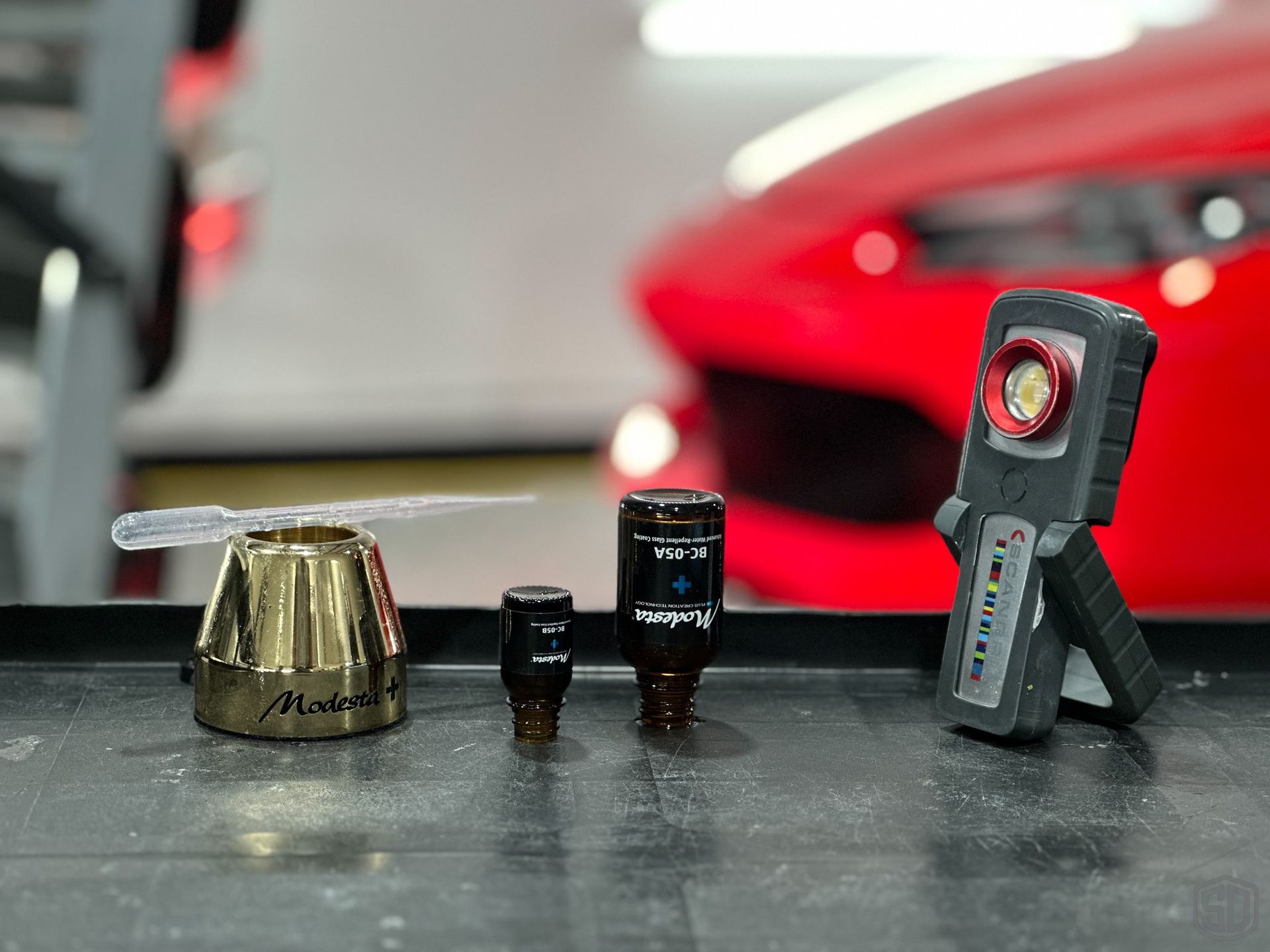 A group of tools are sitting on a table in front of a red car.