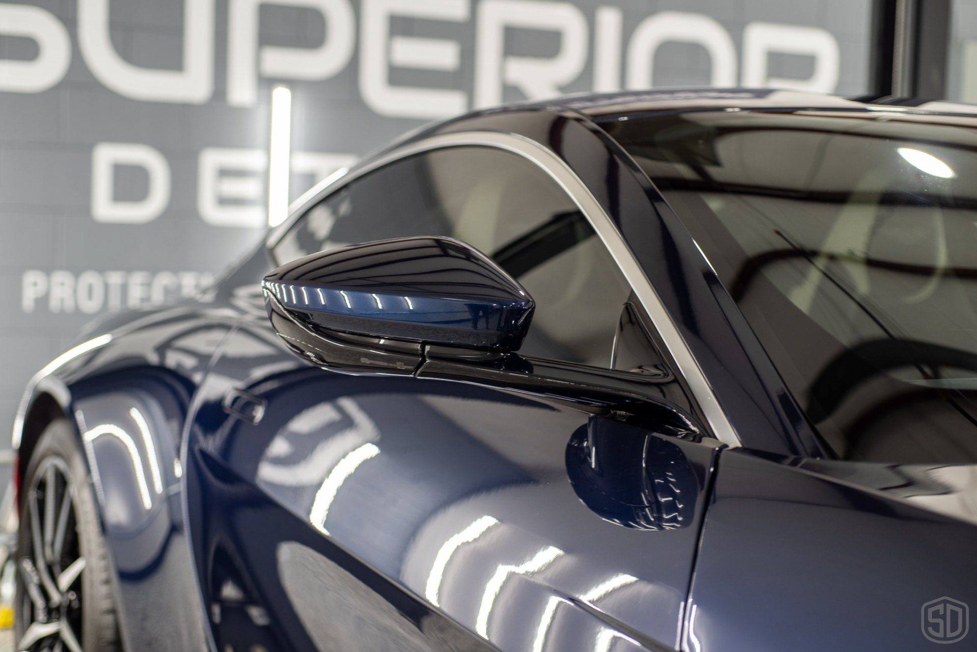 A black sports car is parked in front of a sign that says superior detail.
