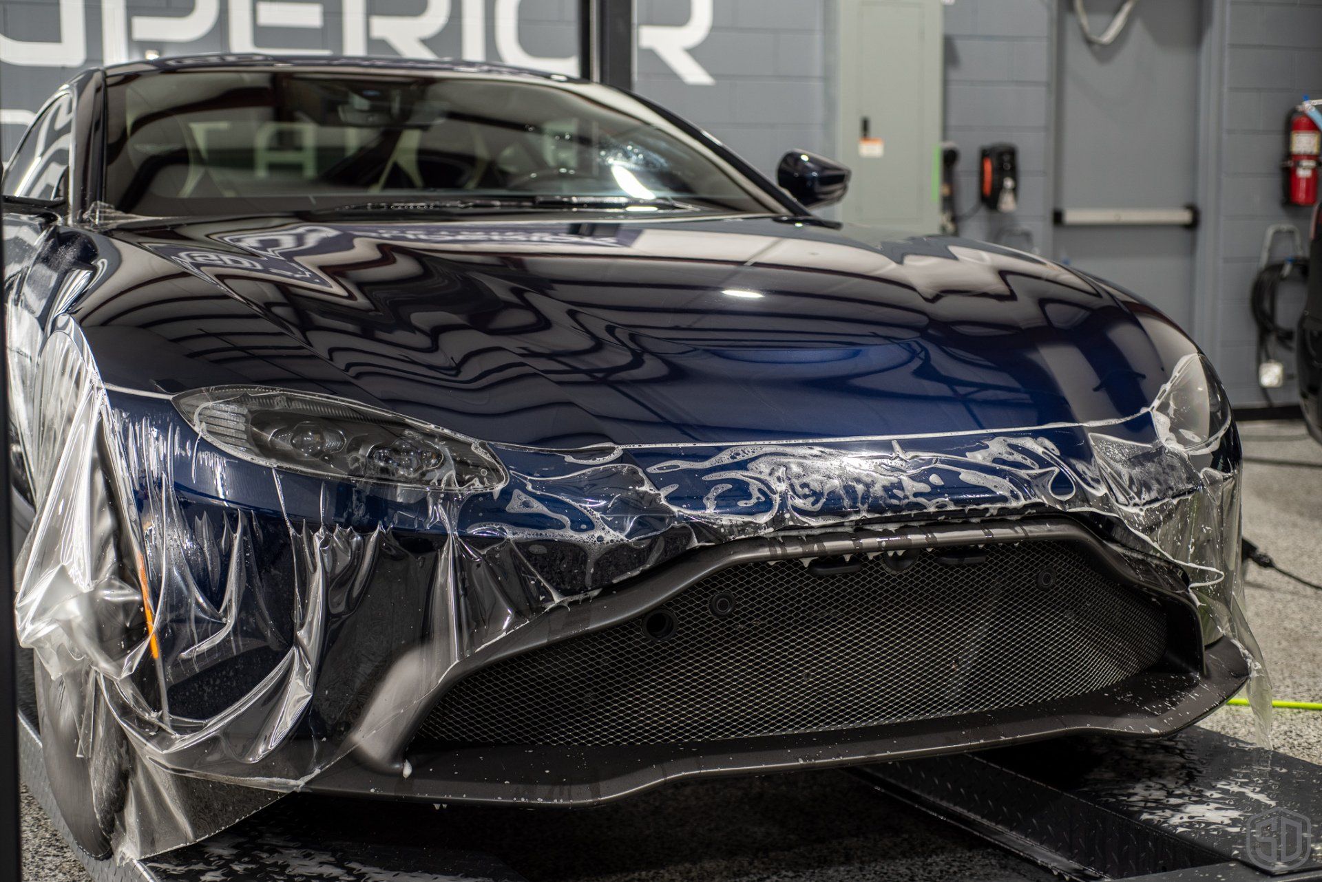 A black sports car is wrapped in plastic in a garage.