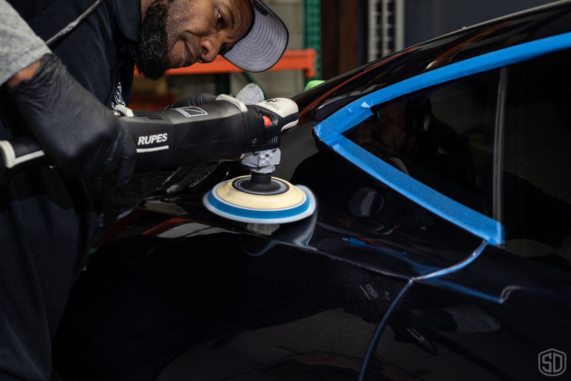 A man is polishing a black car with a machine.