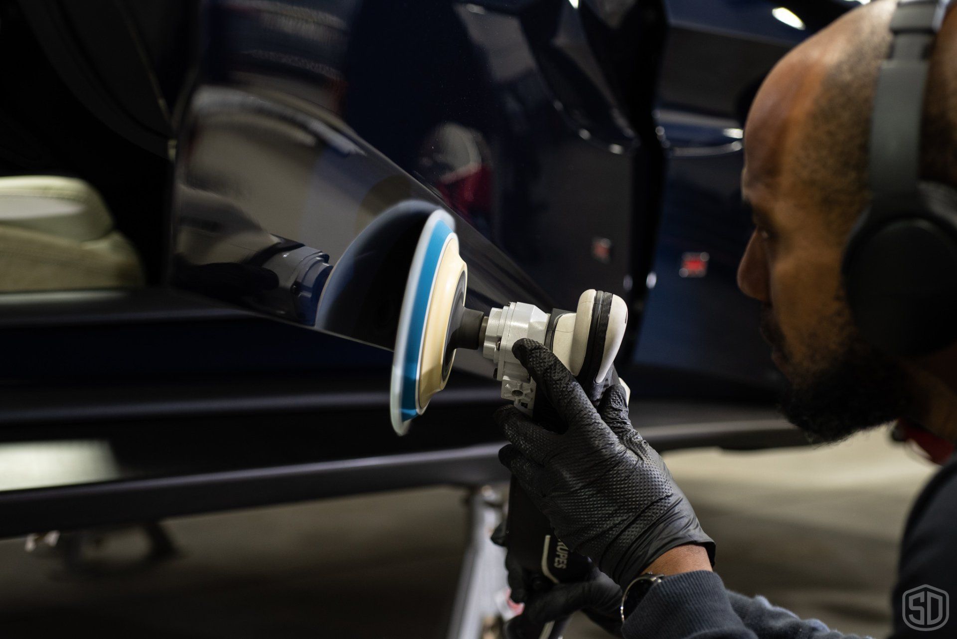 A man wearing headphones is polishing a car with a machine.