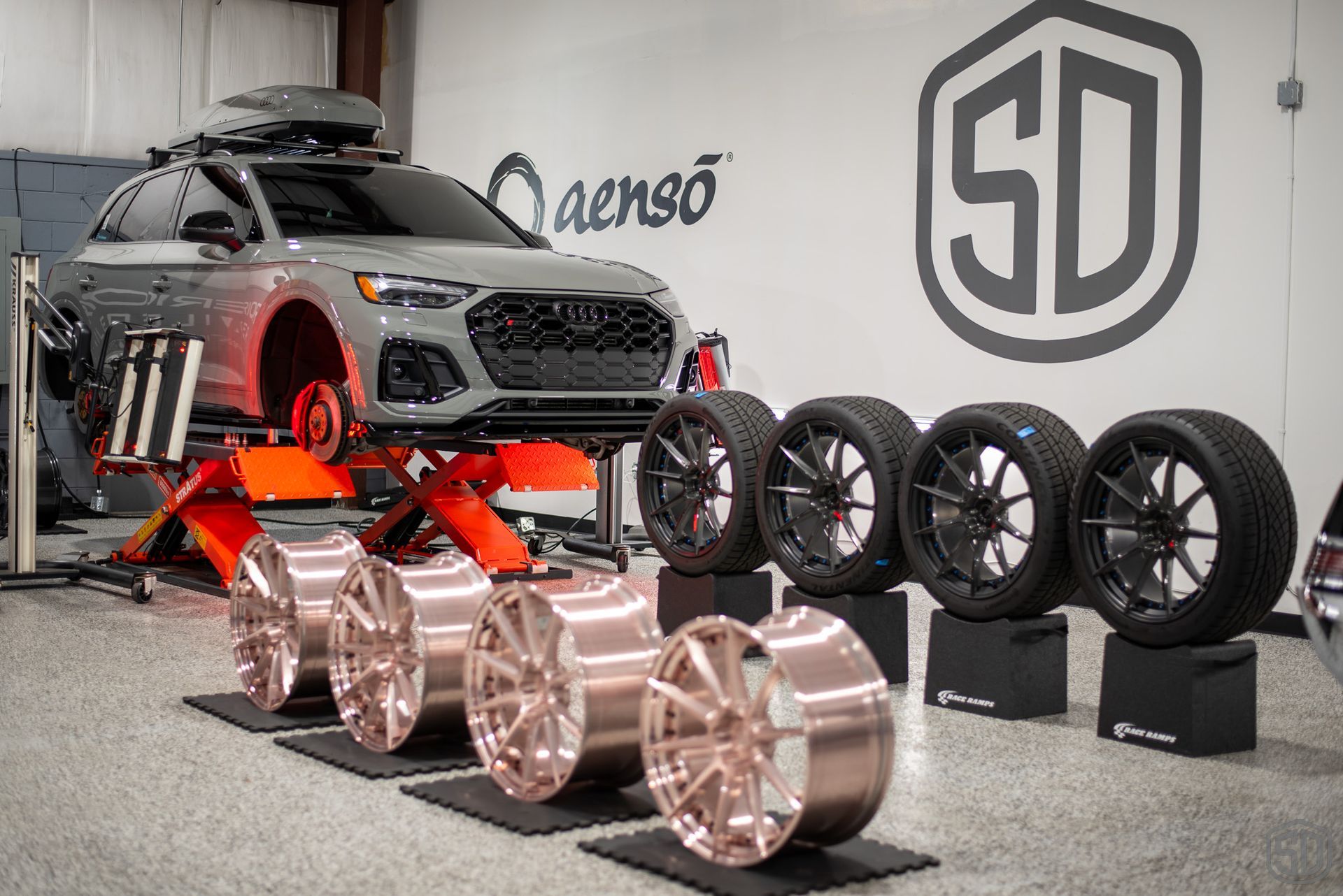 A car is sitting on a lift next to a row of wheels and tires.