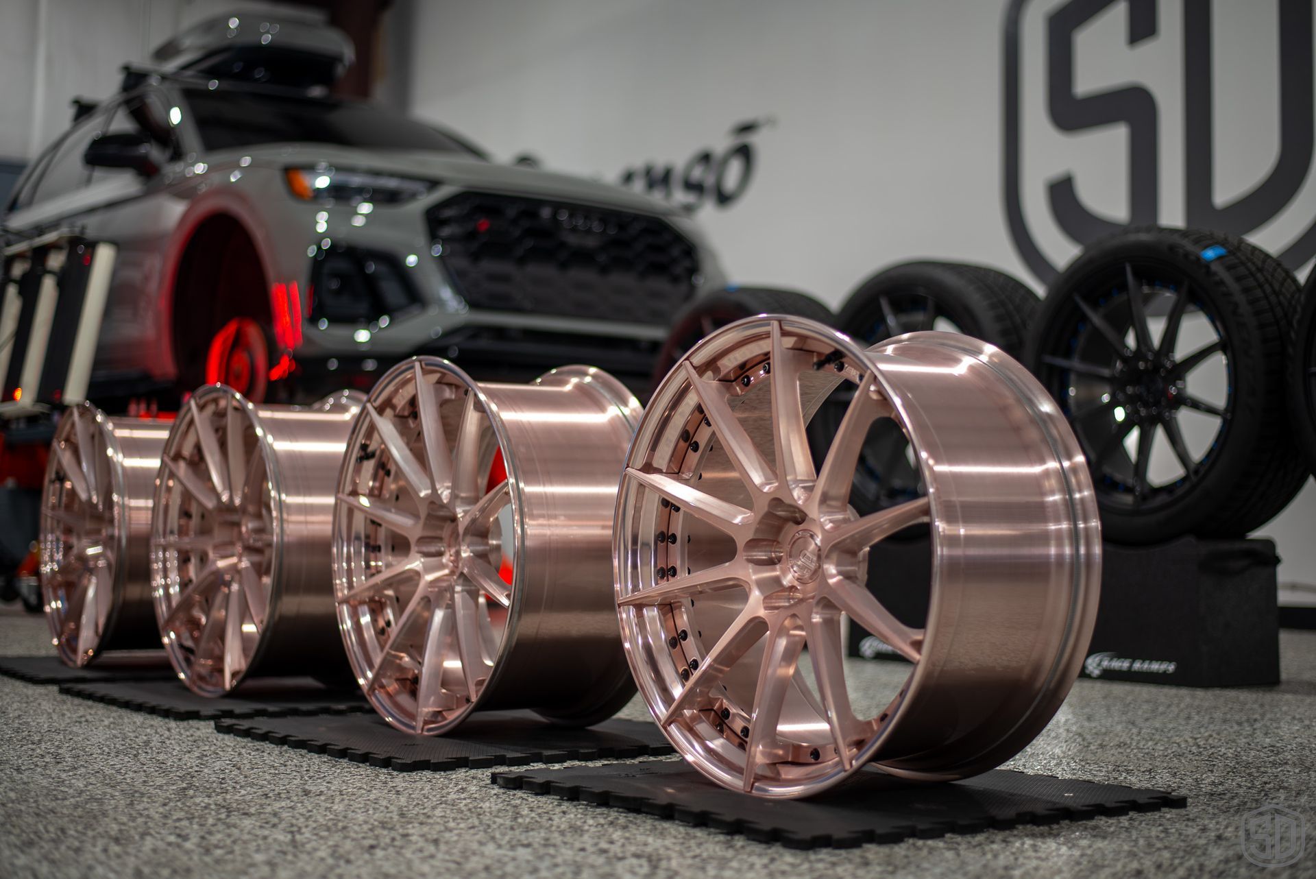 A row of wheels are sitting on a mat in front of a car.