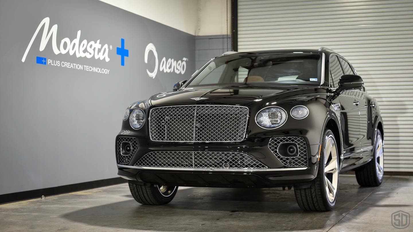 A black bentley bentayga is parked in front of a garage door.