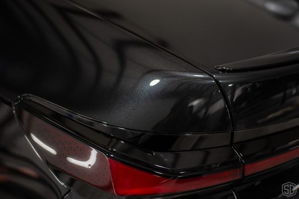 A black car with a red tail light is parked in a garage.