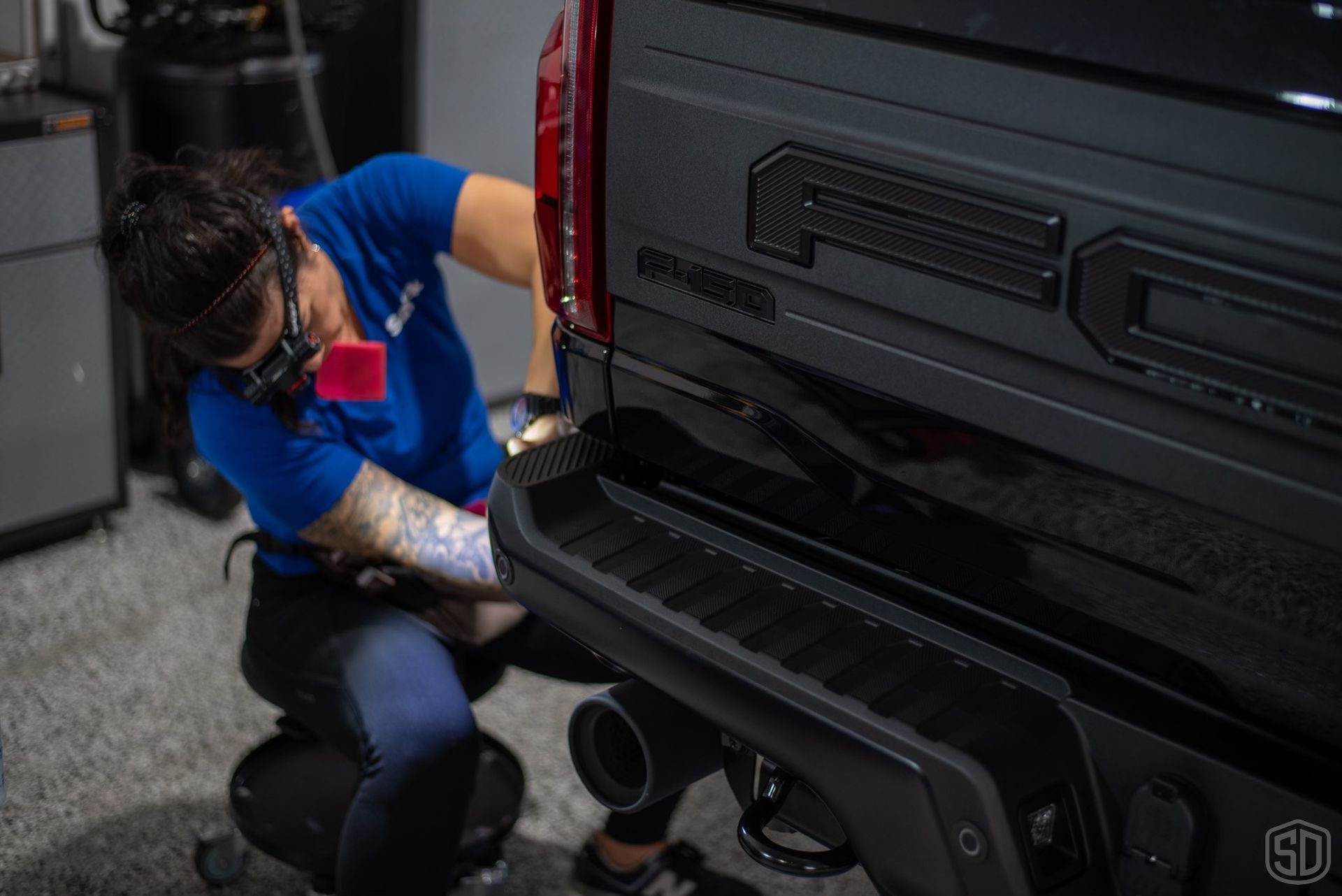 A woman is cleaning the back of a black truck.