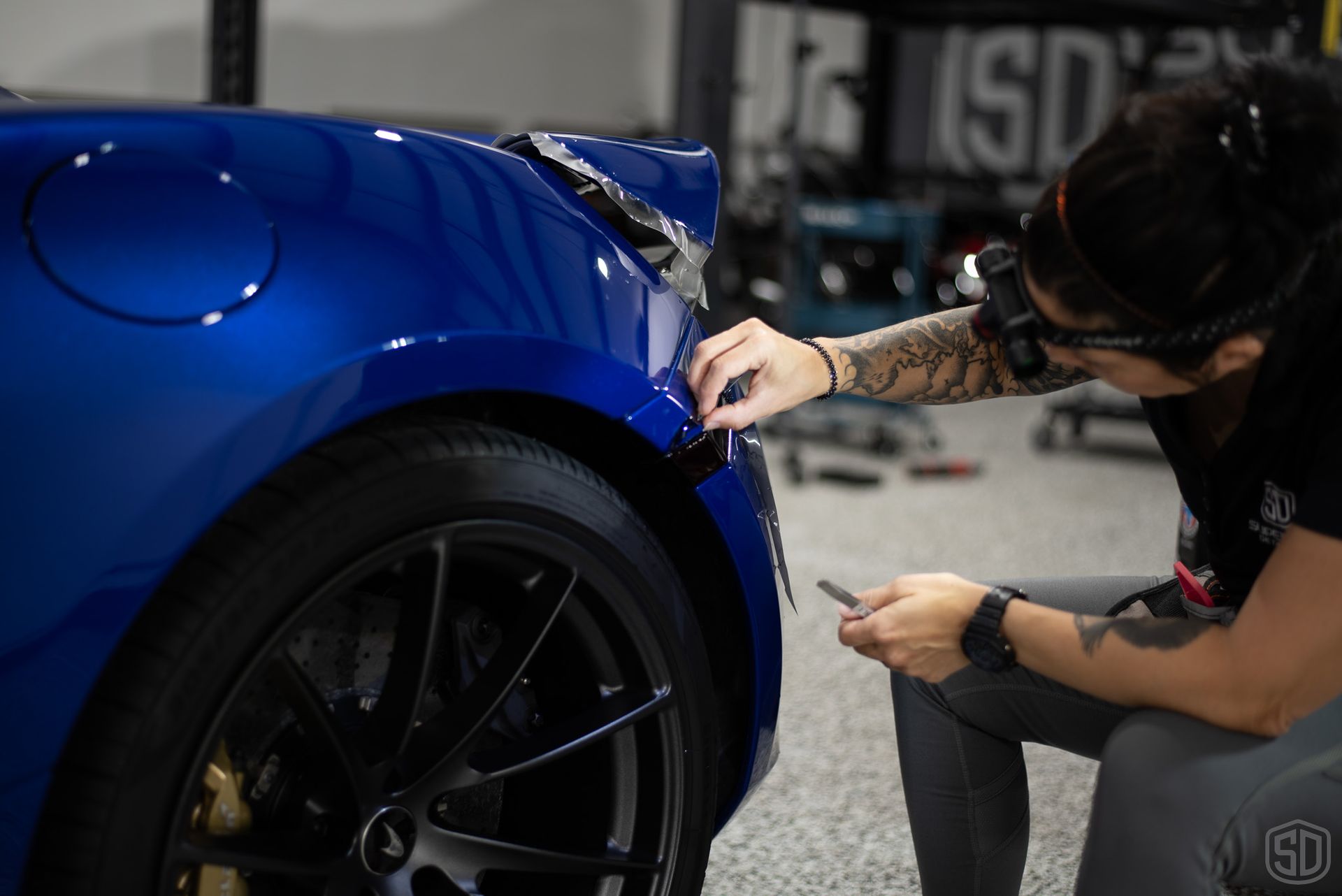 A woman is working on a blue car in a garage.