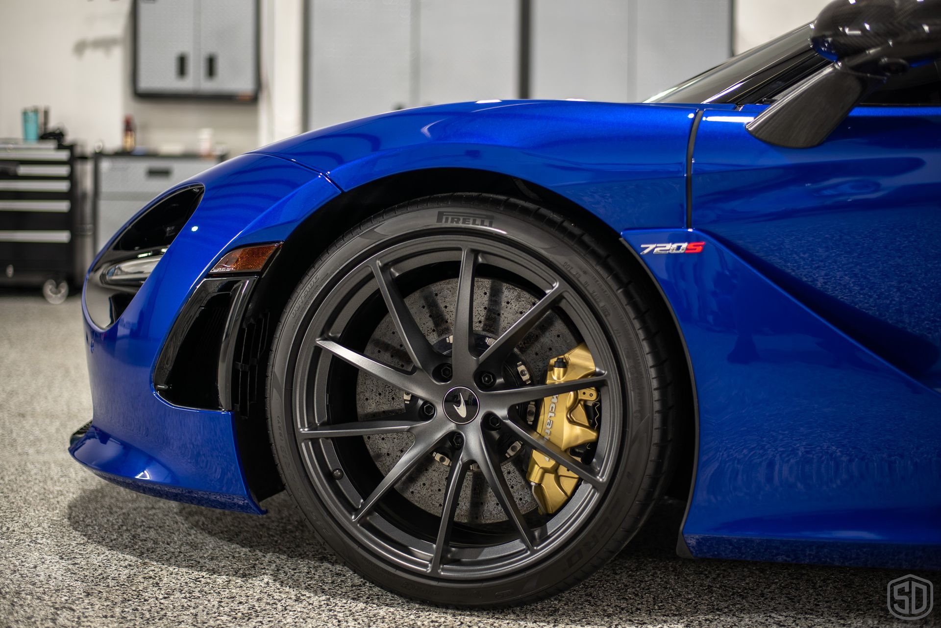 A blue sports car with black wheels is parked in a garage.