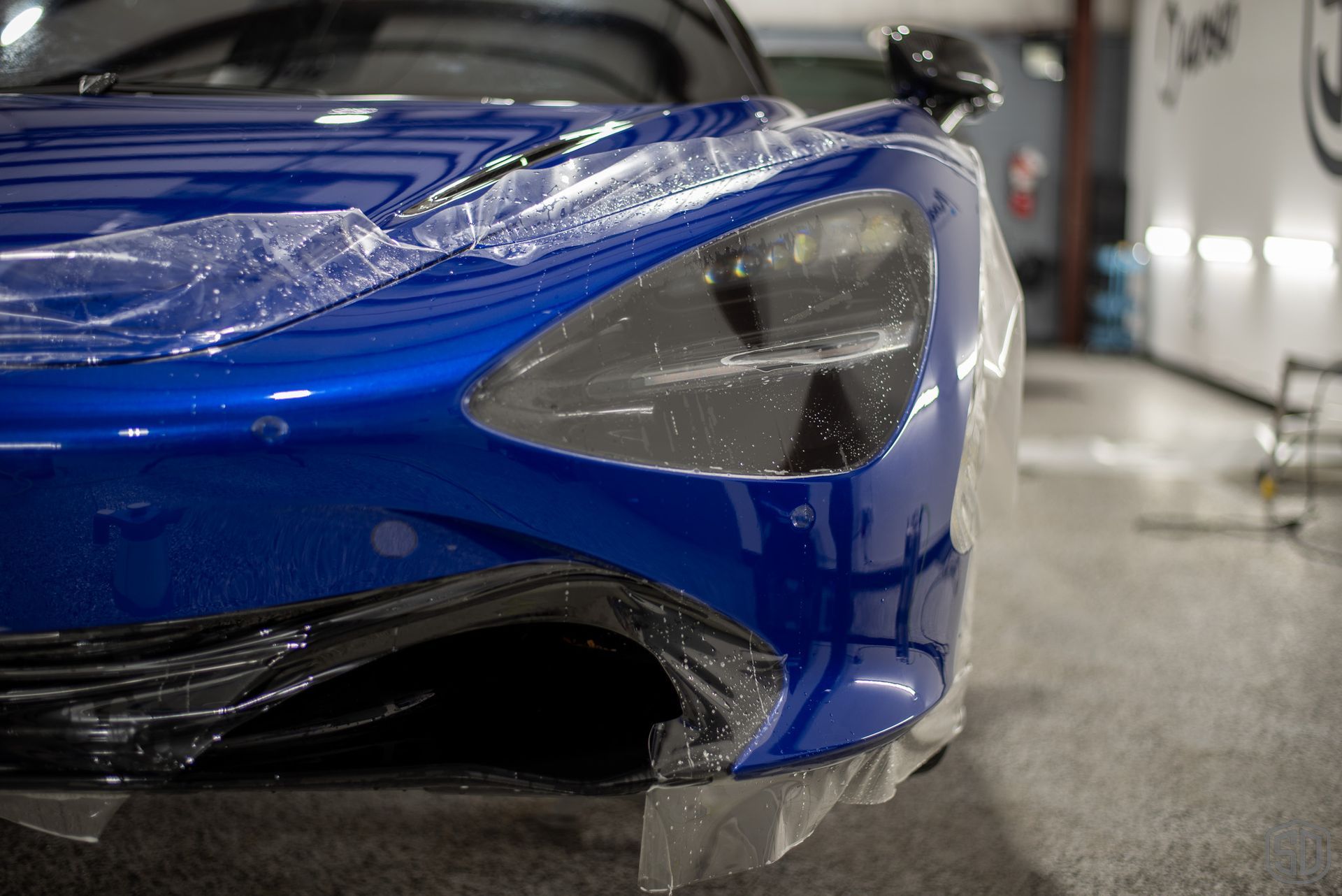 A blue sports car is wrapped in plastic in a garage.
