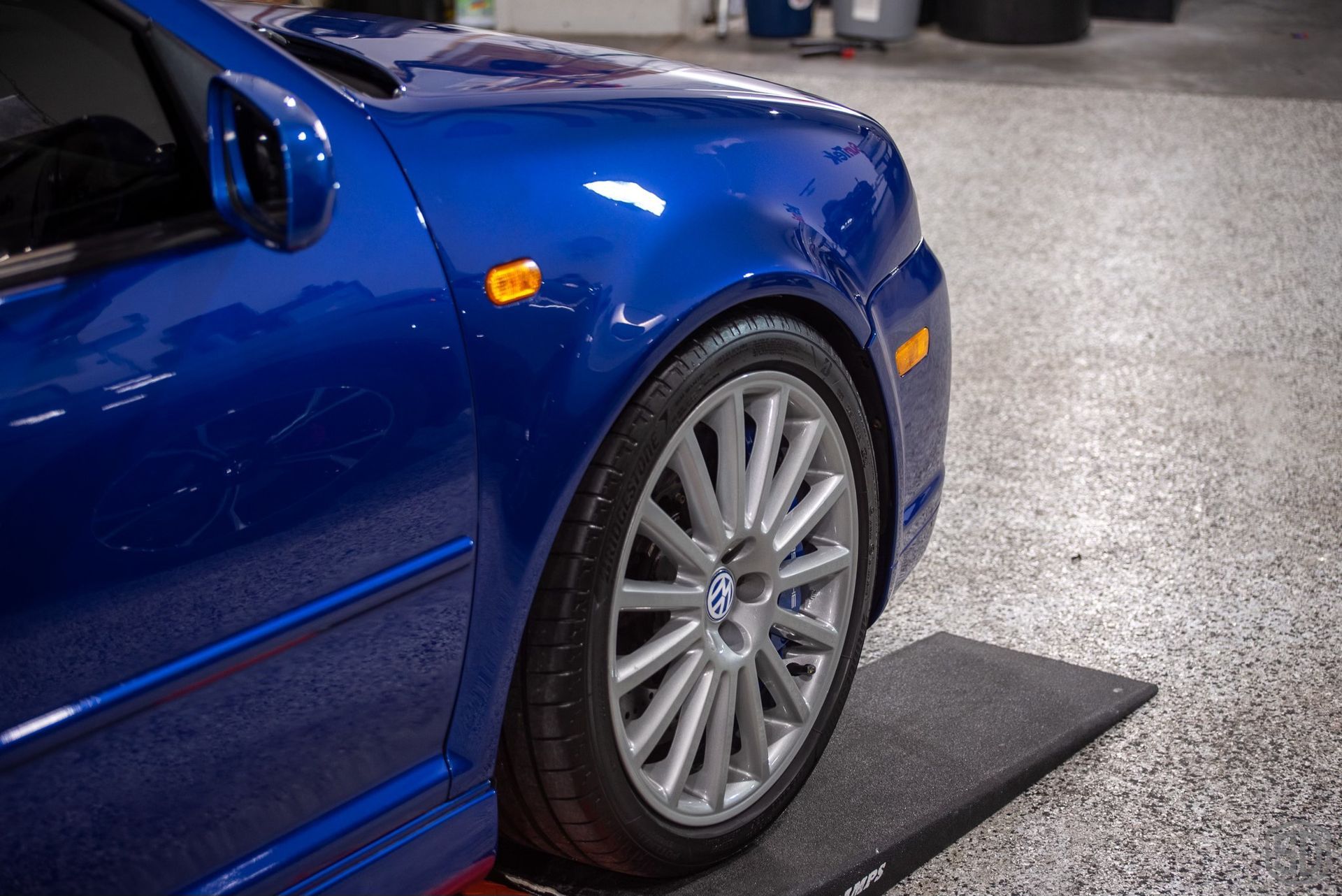 A blue car is parked on a black mat in a garage.