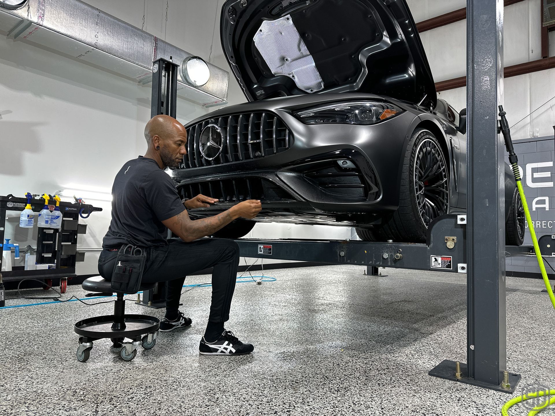 A man is working on a car in a garage with the hood up.