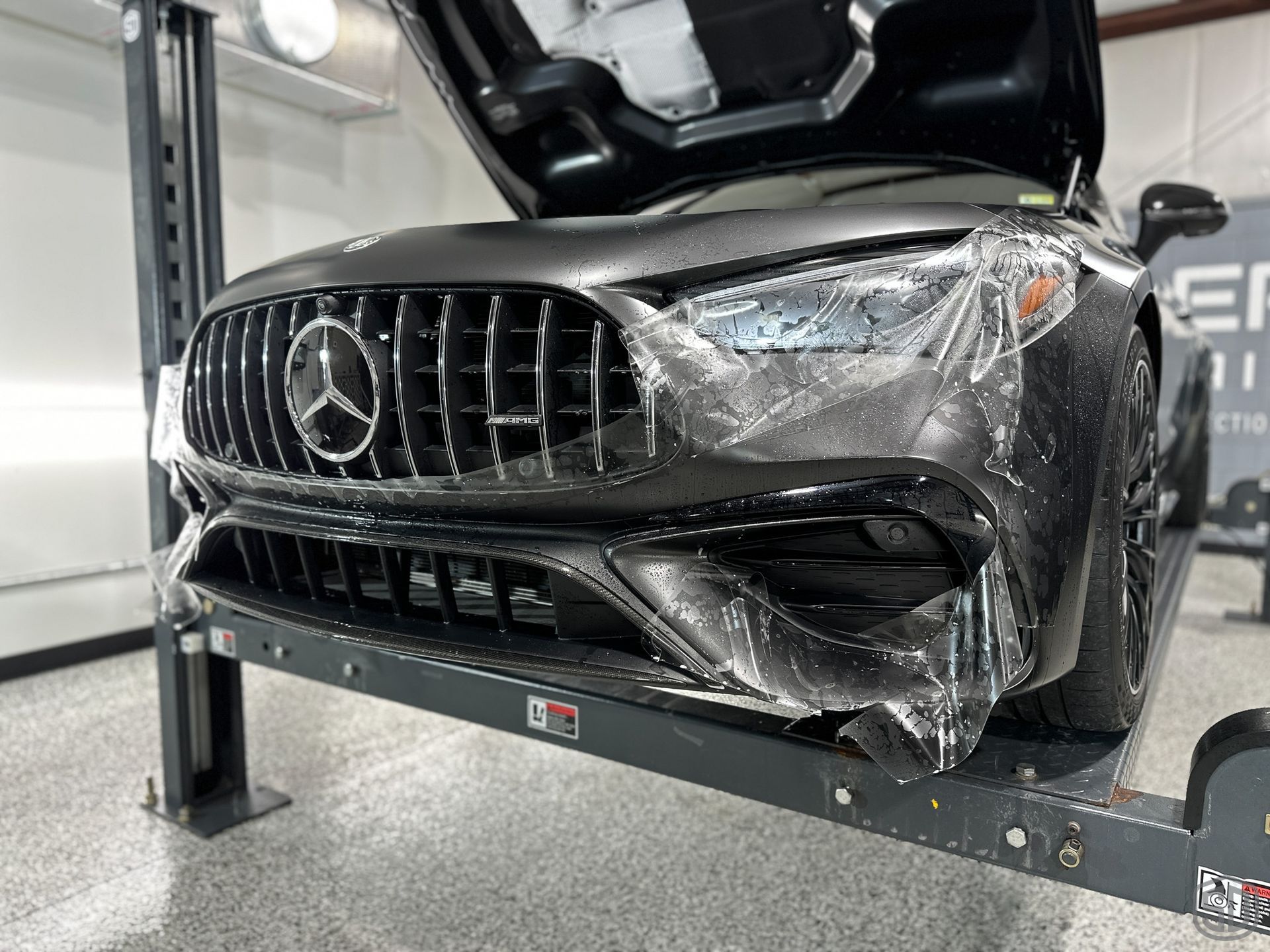 A mercedes benz is wrapped in plastic and sitting on a lift.