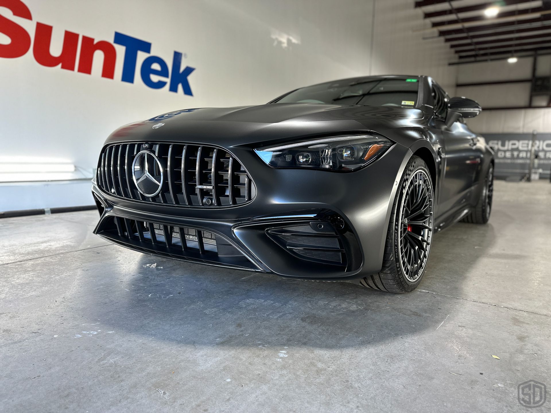 A black sports car is parked in front of a suntek sign.