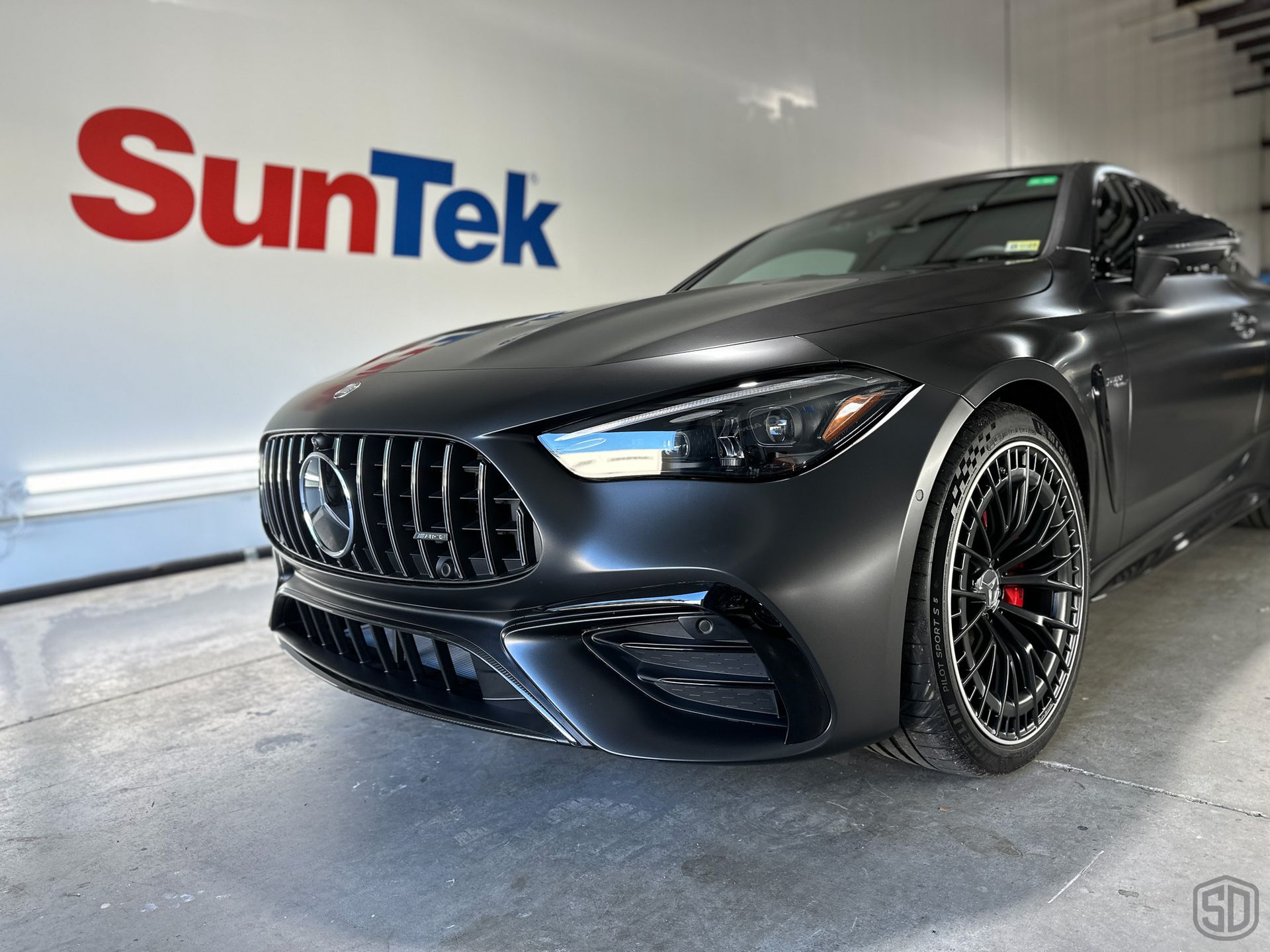 A black car is parked in front of a suntek sign.