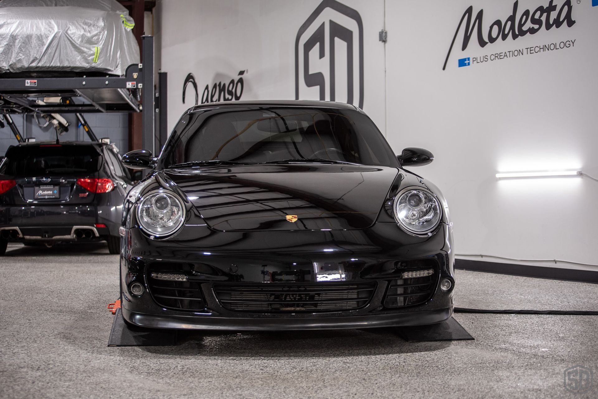 A black porsche 911 turbo is parked in a garage.