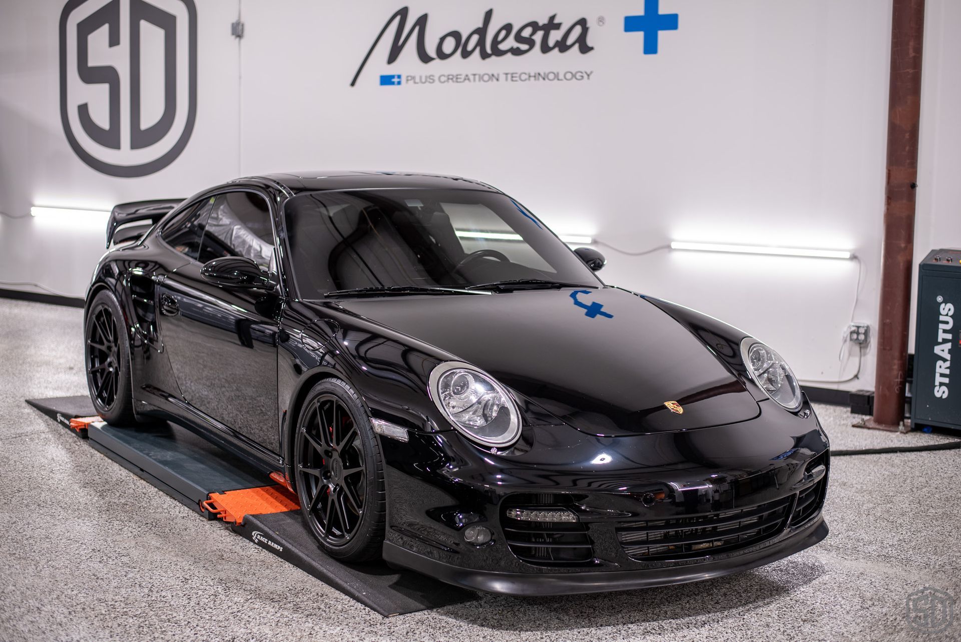 A black porsche 911 turbo is parked on a lift in a garage.