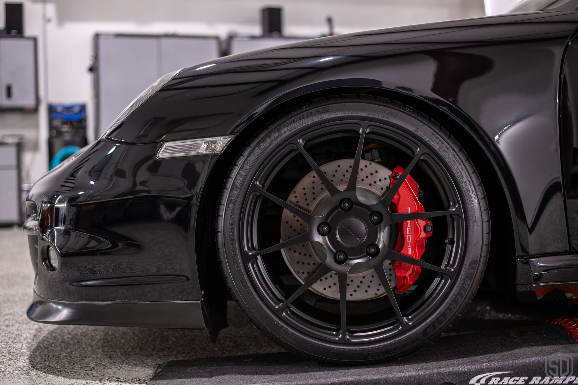 A black sports car with red brake calipers is parked in a garage.