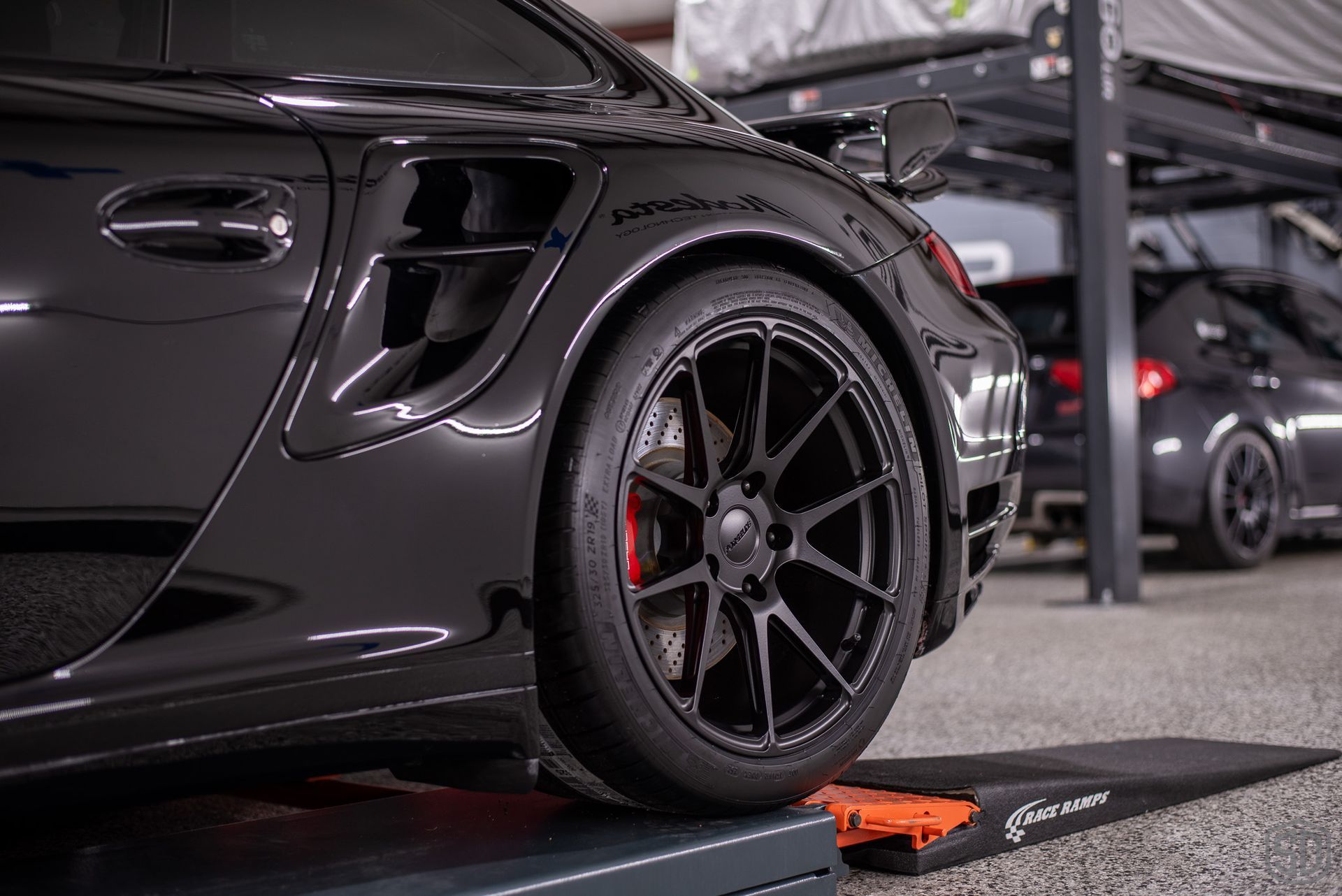 A black sports car is sitting on top of a ramp in a garage.