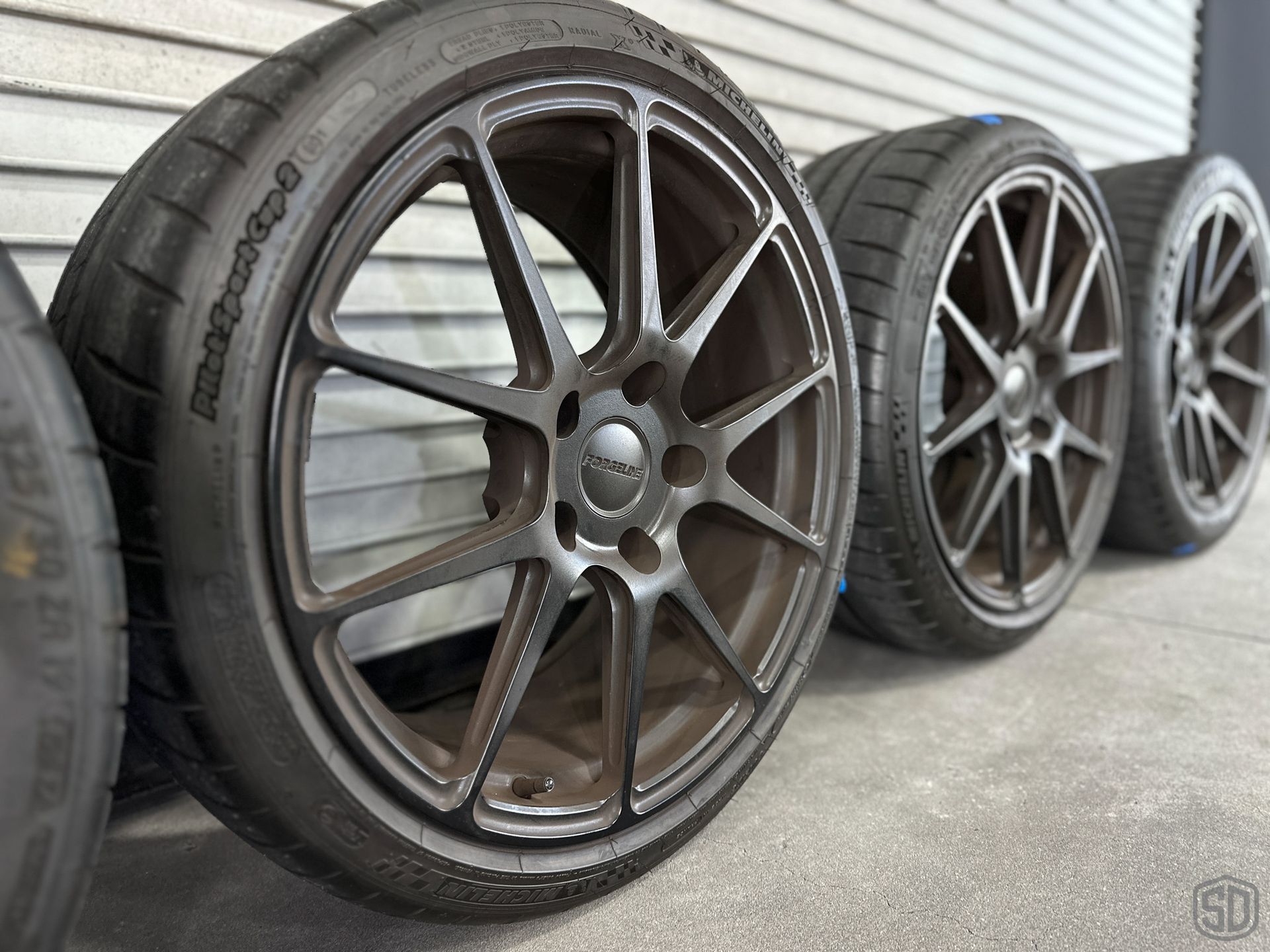 A row of tires and wheels are lined up against a wall