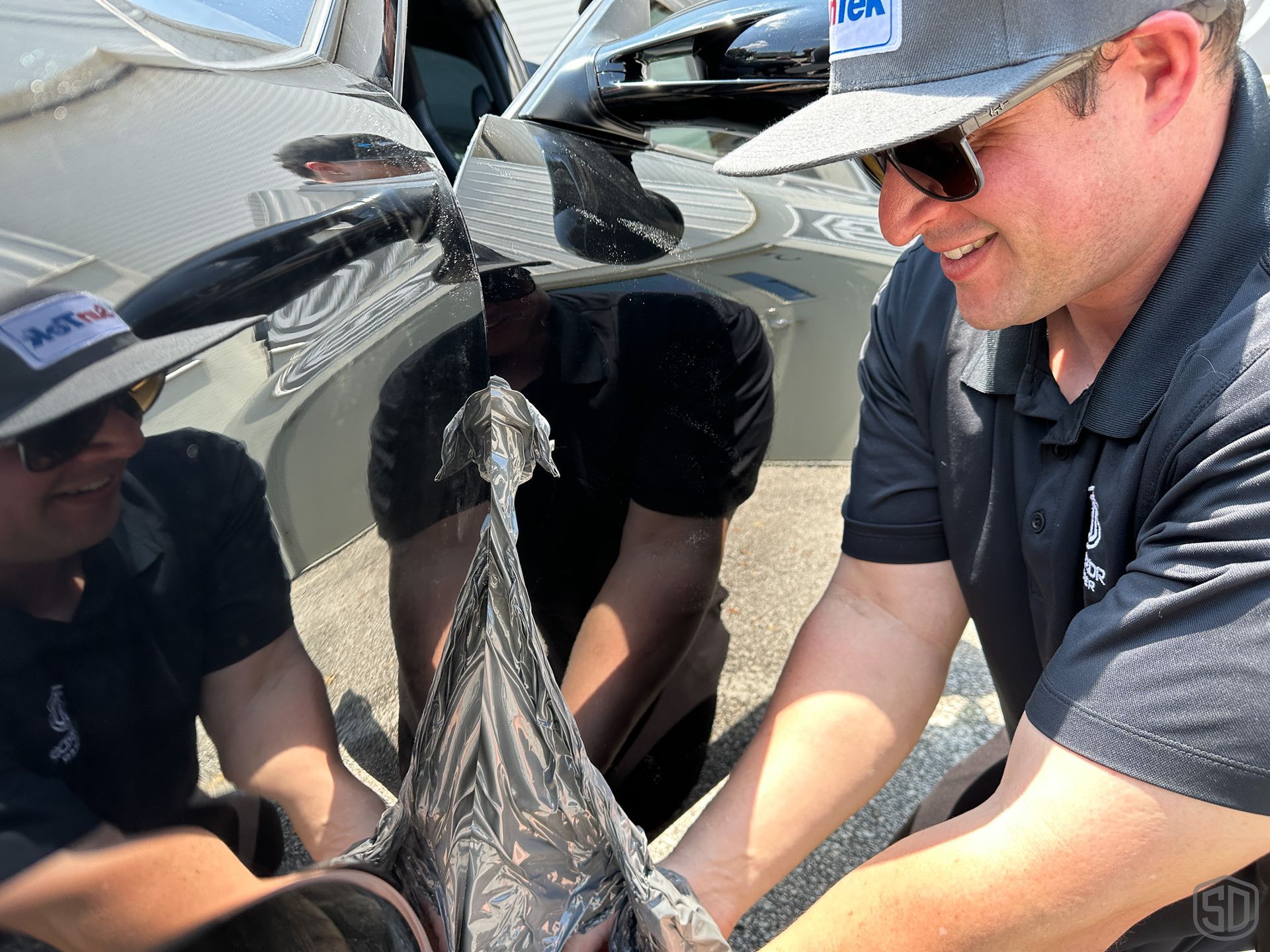 A man wearing a hat and sunglasses is holding a bag in front of a car.