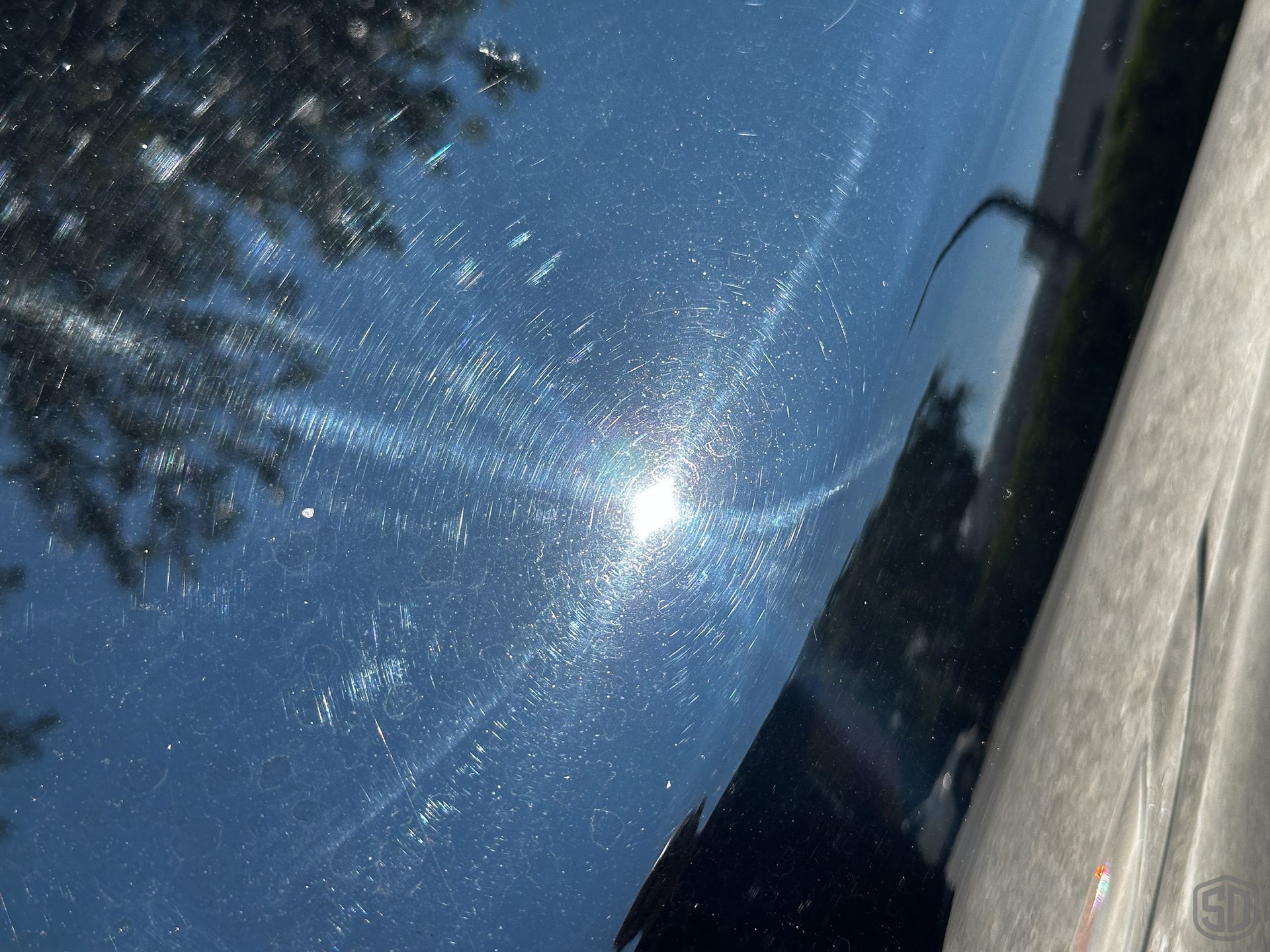 The sun is reflected on a black Porsche 911 Turbo, revealing water marks, scratches, & other damage