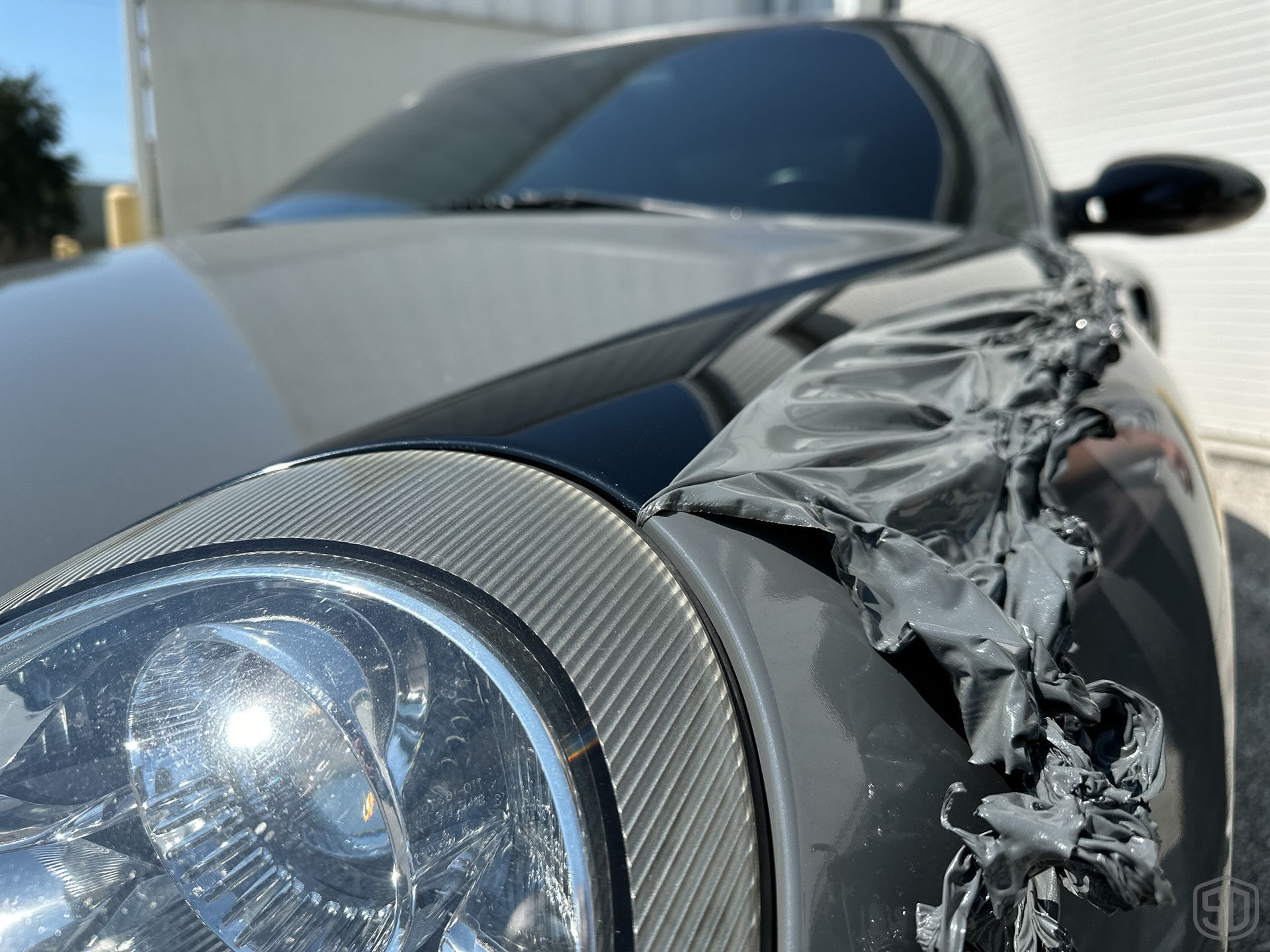 A black car with a damaged fender and headlight