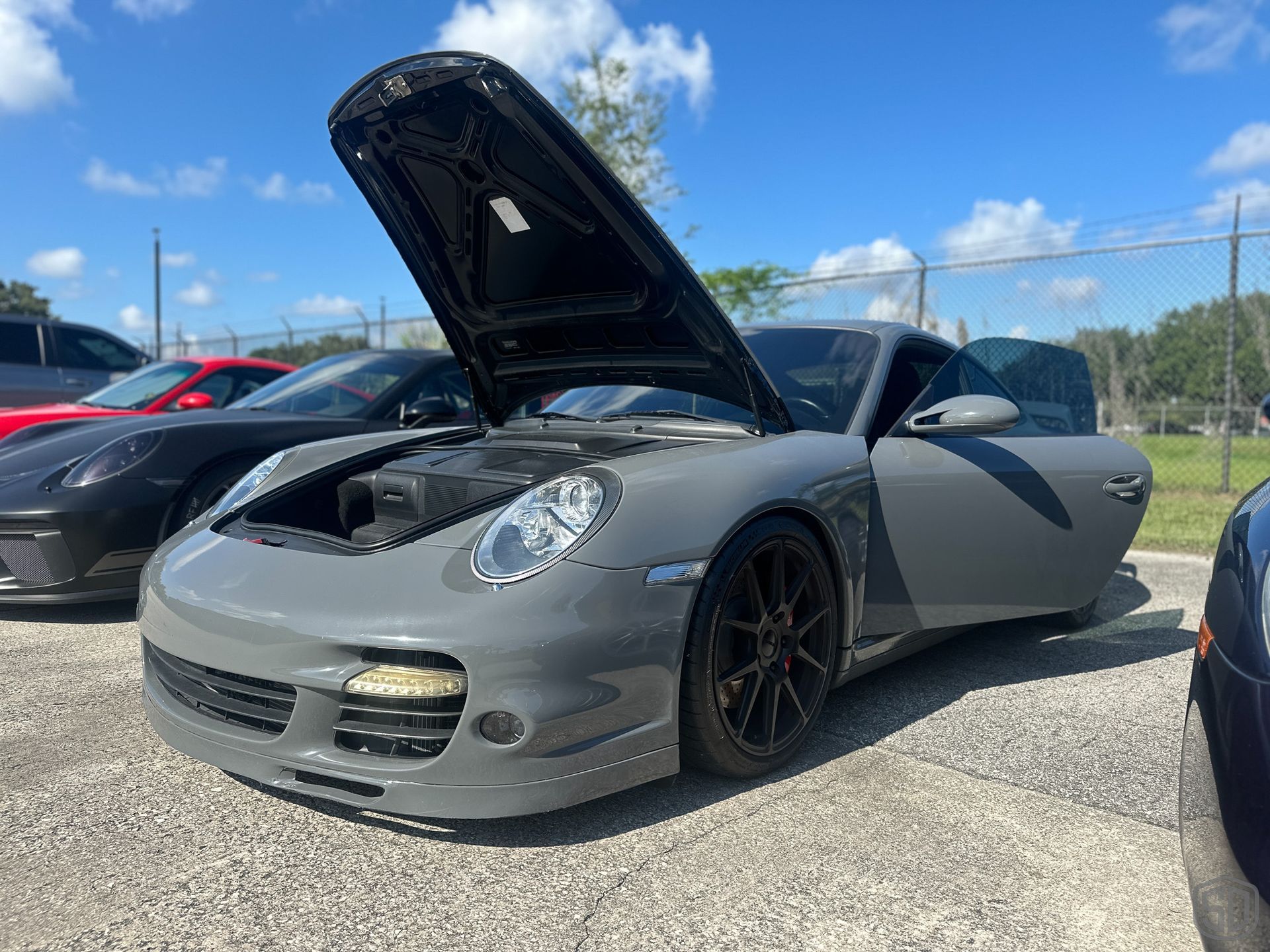 A gray porsche 911 with the hood up is parked in a parking lot.
