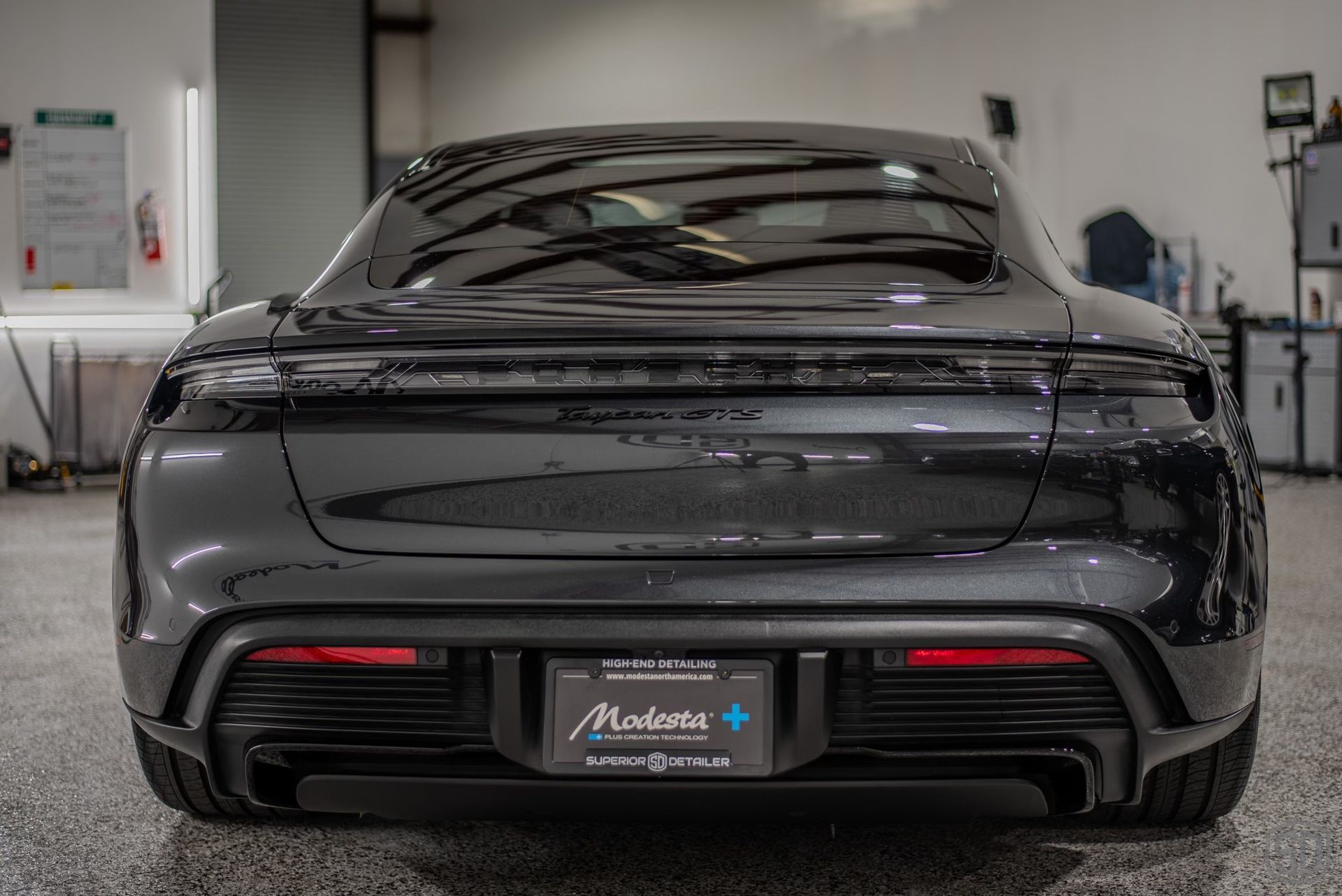 A black porsche taycan is parked in a garage.