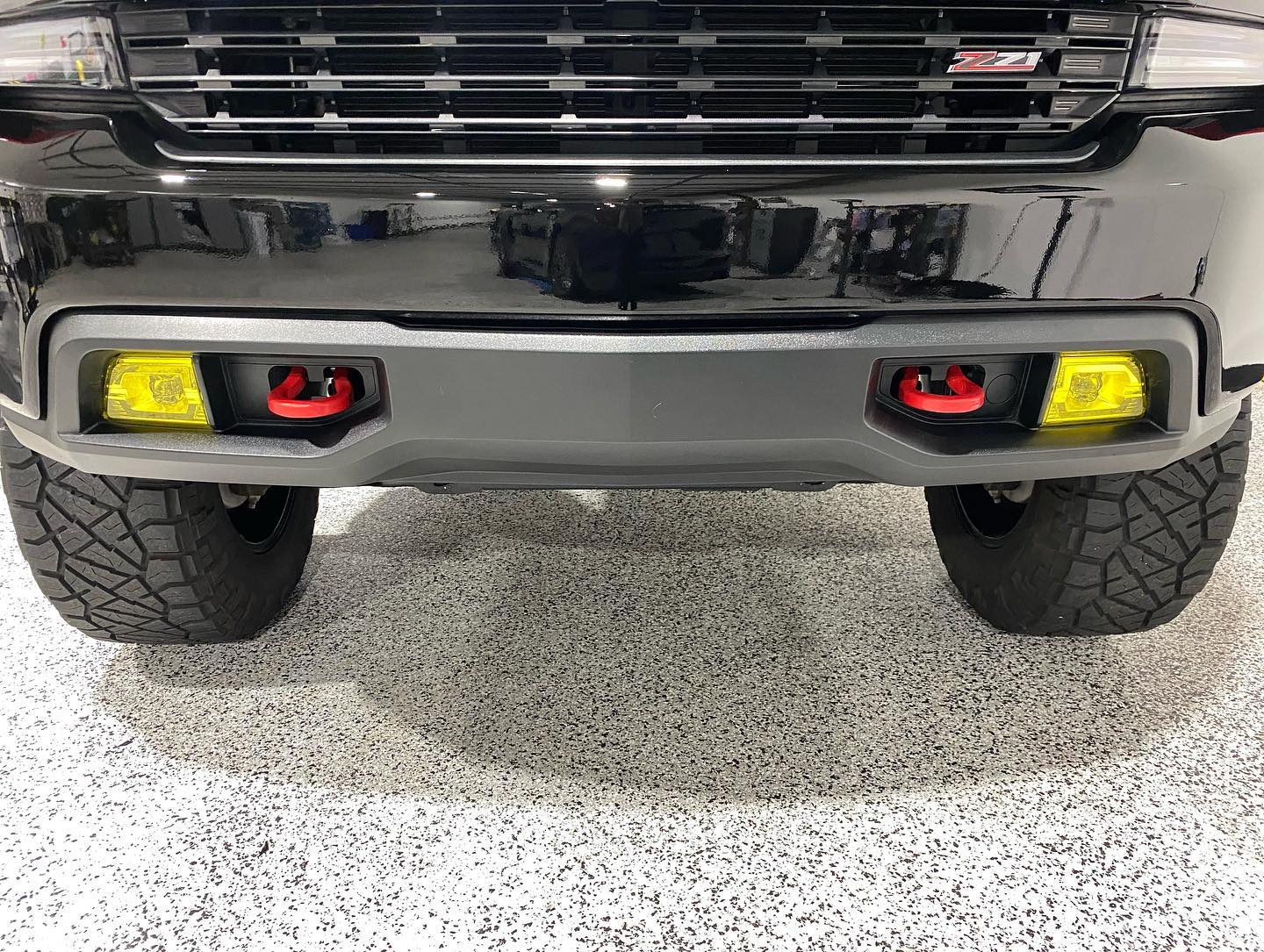 A black truck with yellow lights on the front bumper is parked in a garage.
