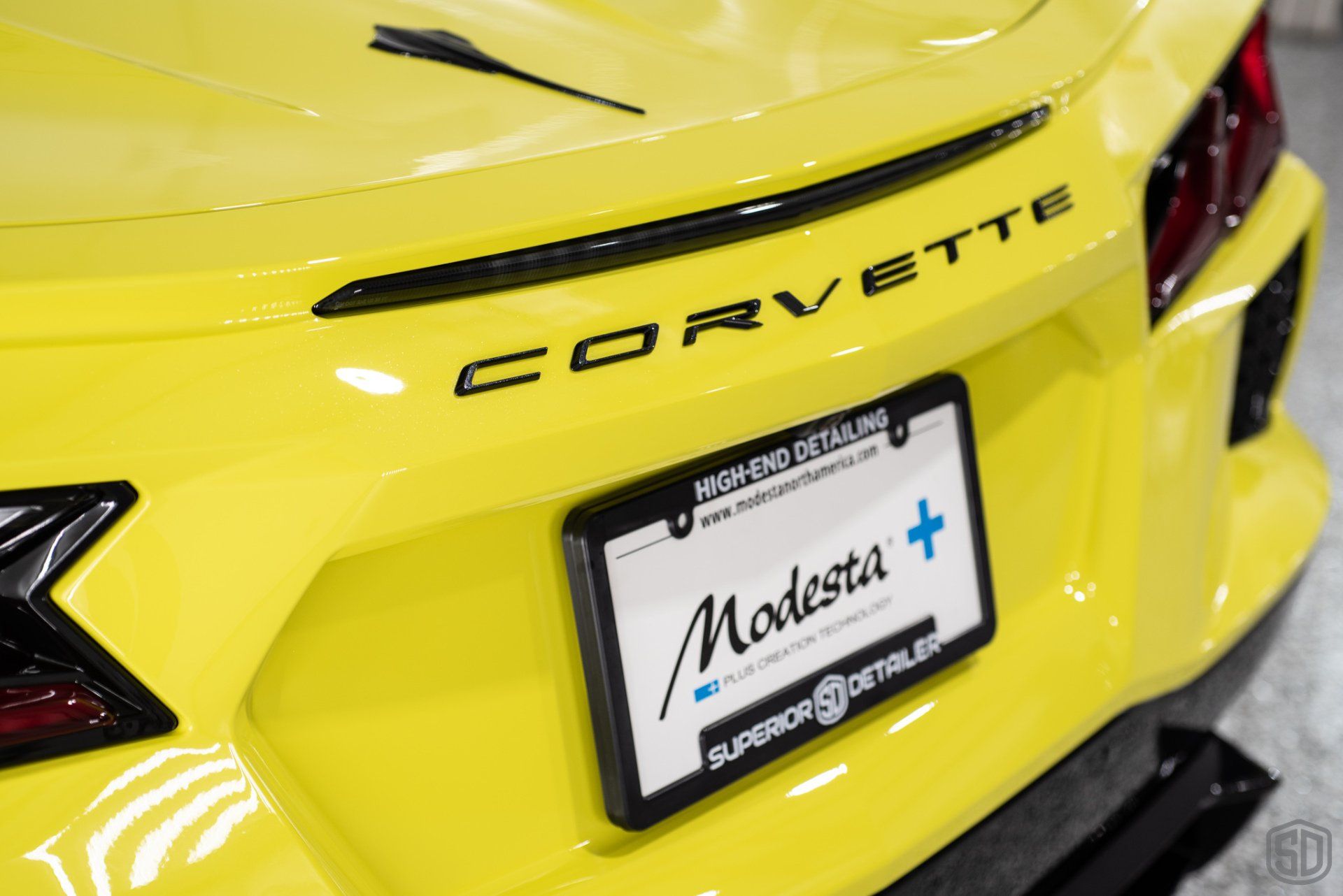 The back of a yellow corvette with a license plate frame.