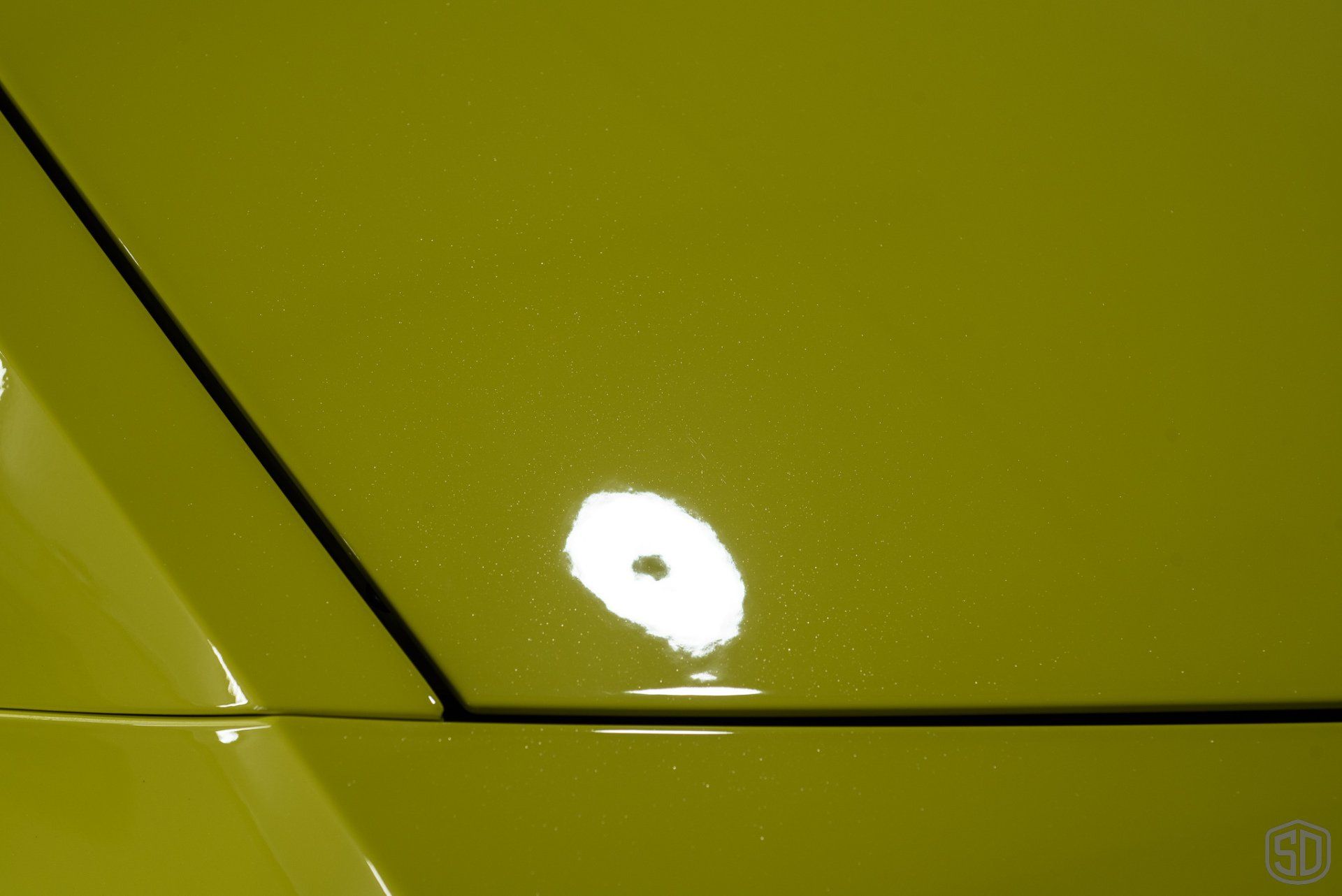 A close up of a yellow car hood with a white spot on it.