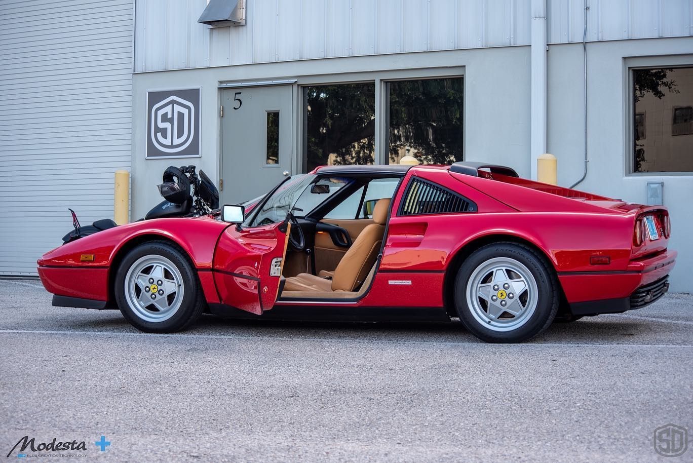A red sports car is parked in front of a building with the door open.