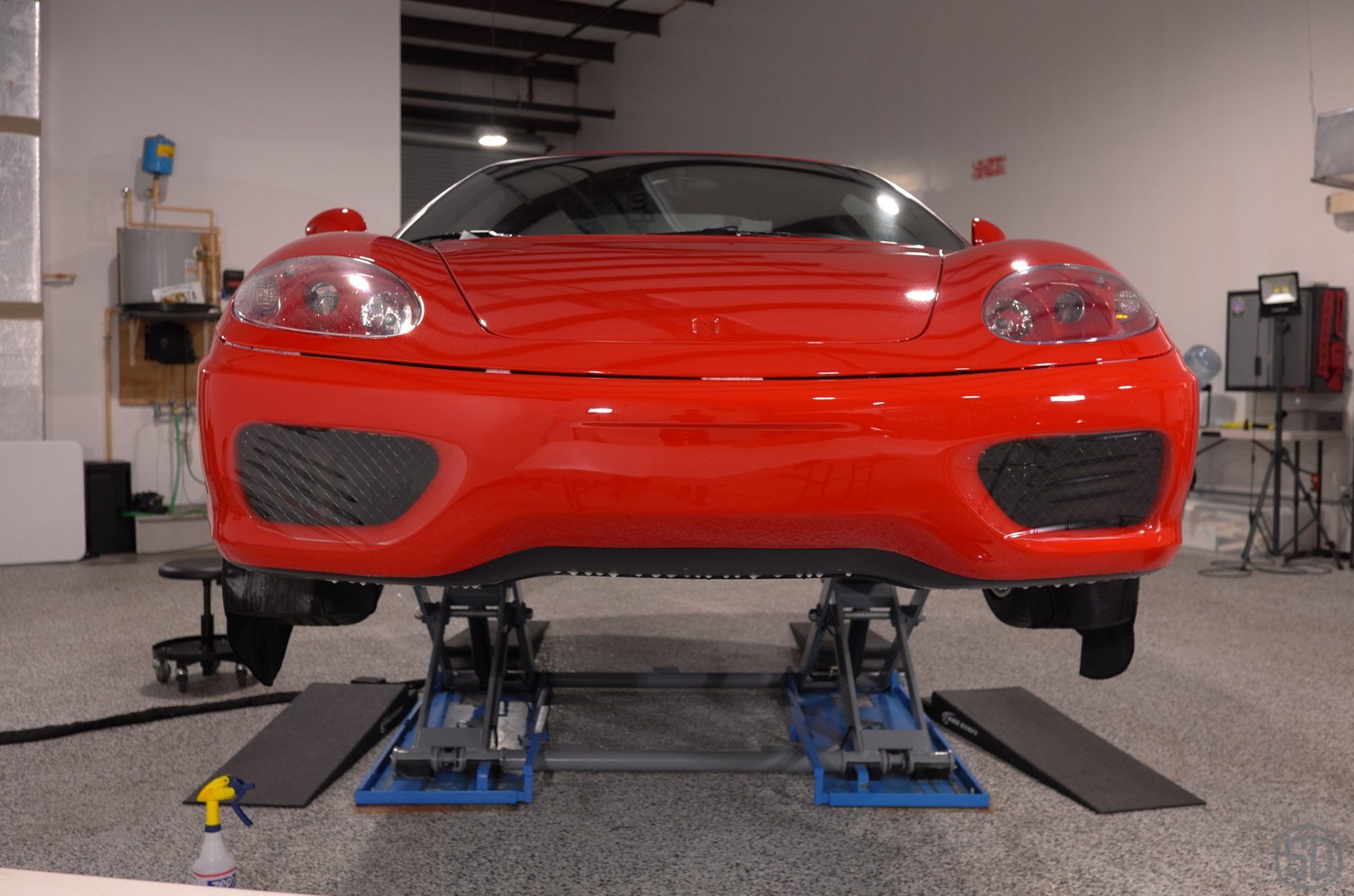 A red sports car is on a lift in a garage