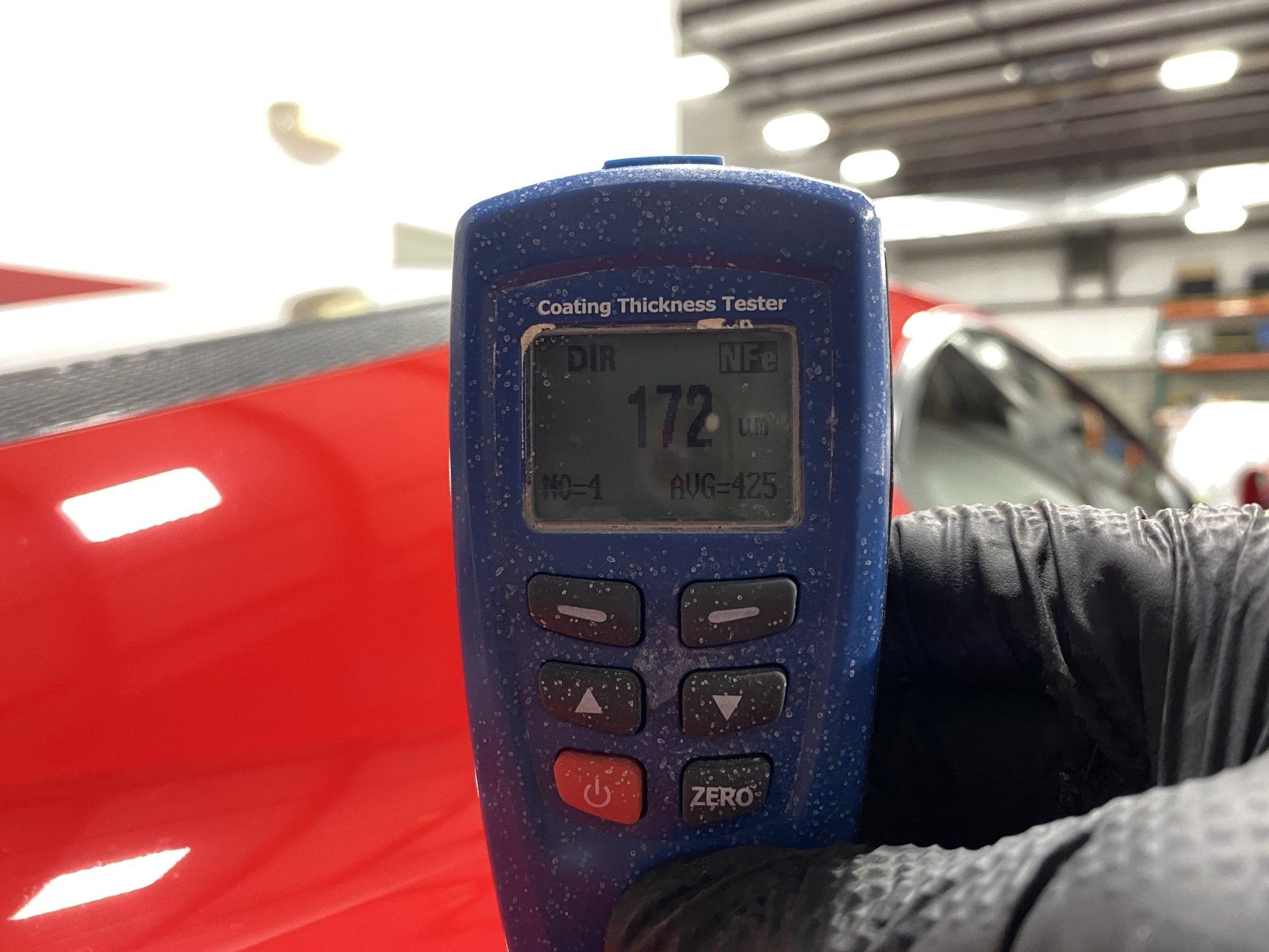 A person is holding a digital gauge in front of a red car.