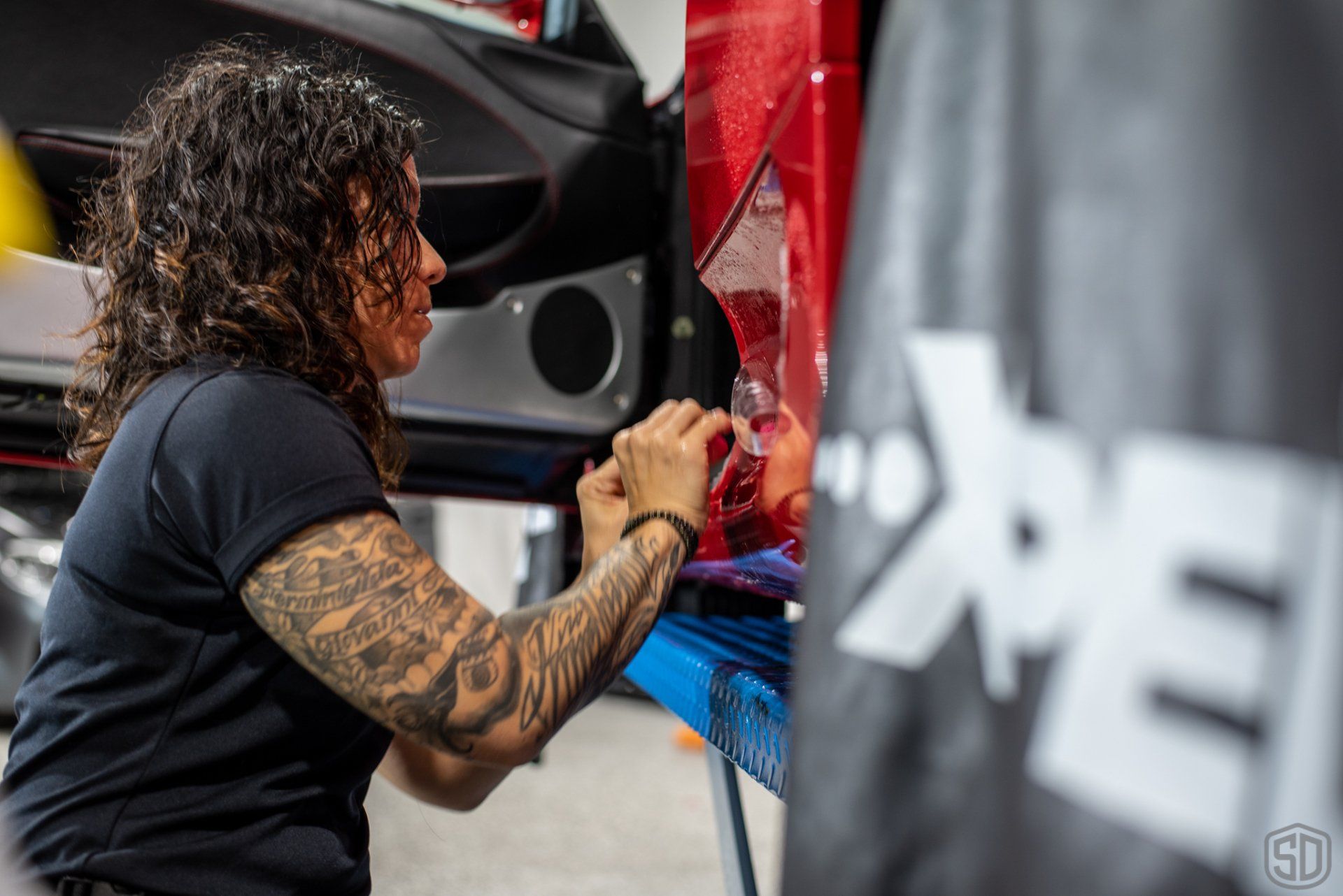 A woman with tattoos is working on a car door.