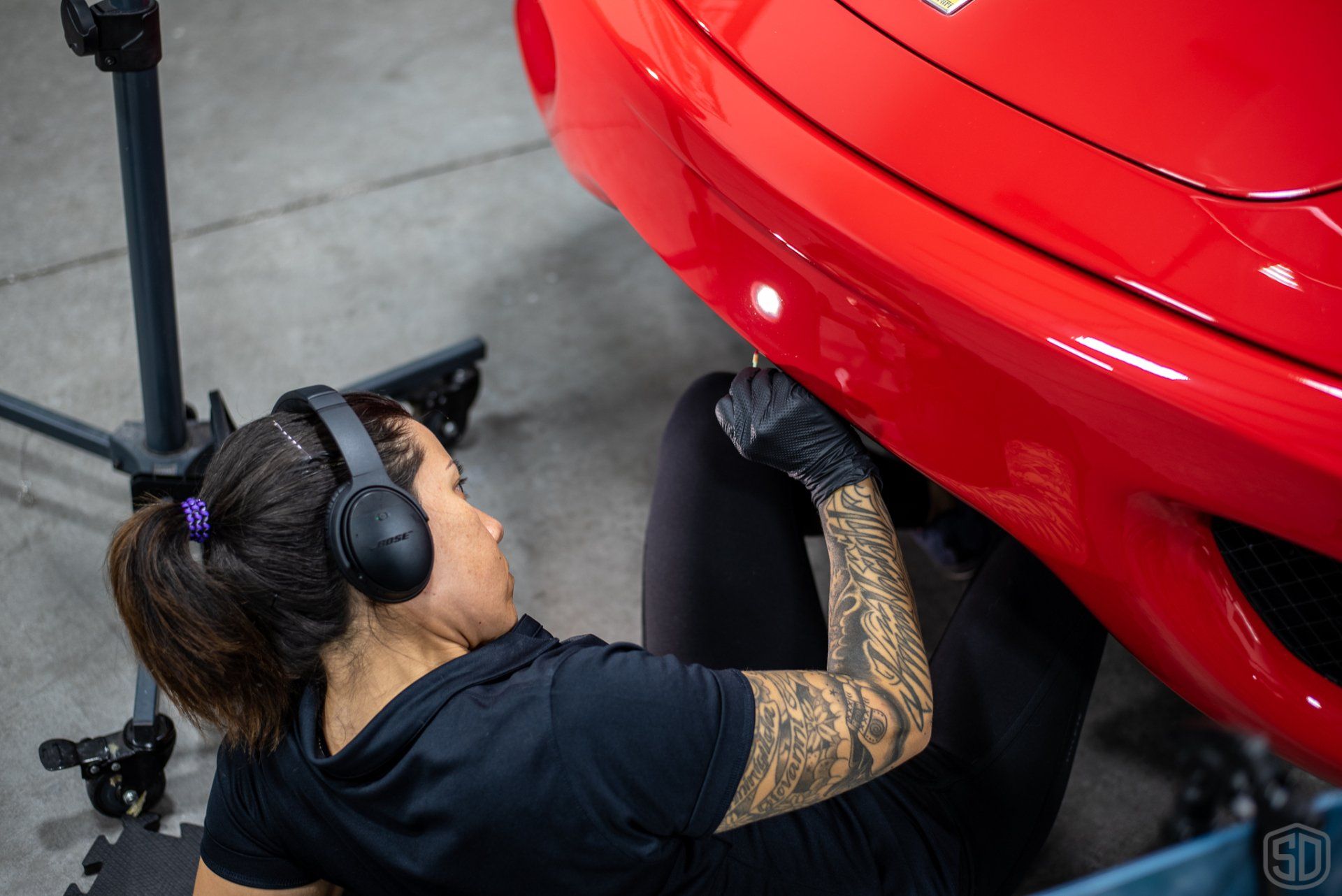 A woman wearing headphones is working on a red car.