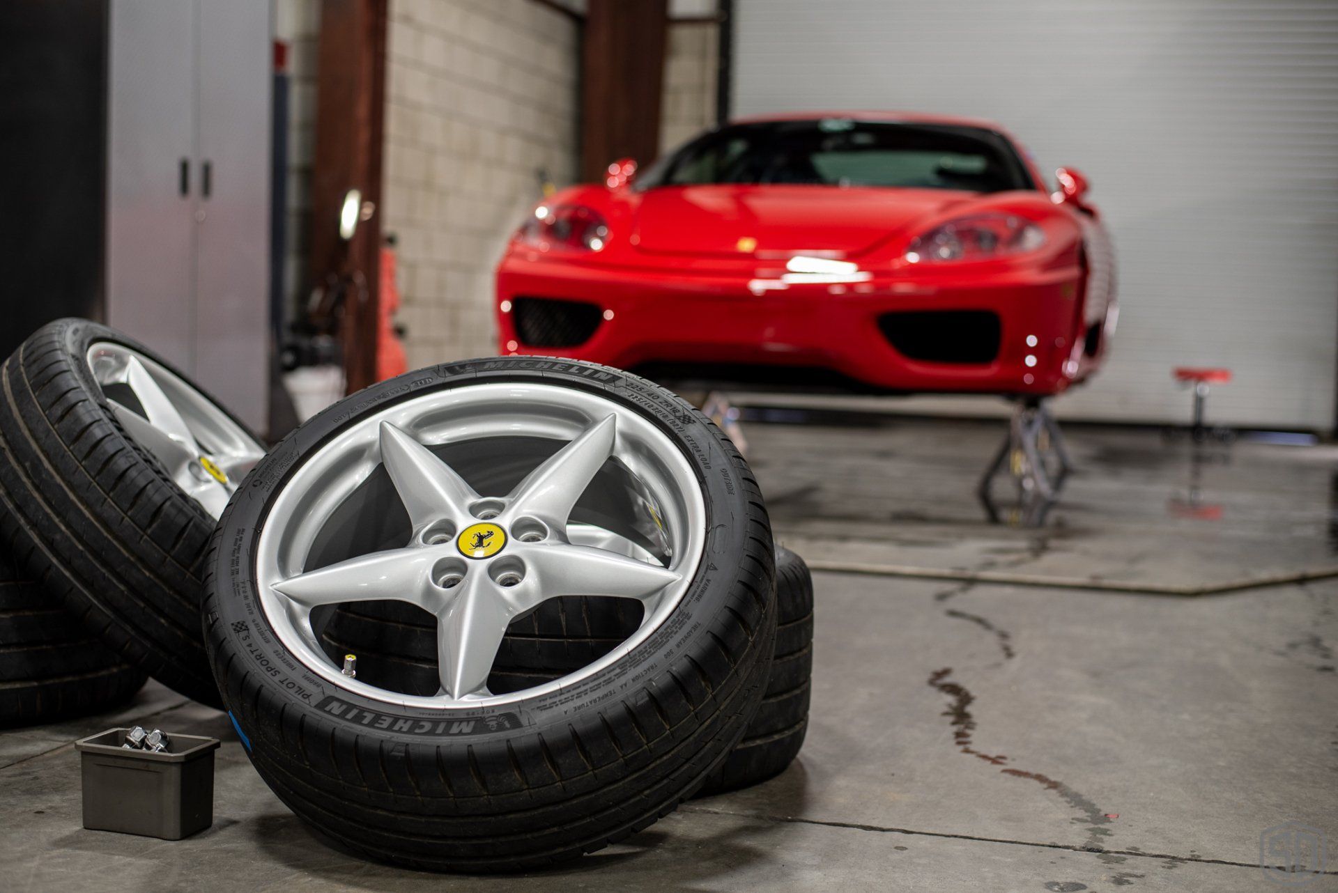 A red ferrari is parked in a garage next to a pile of tires.
