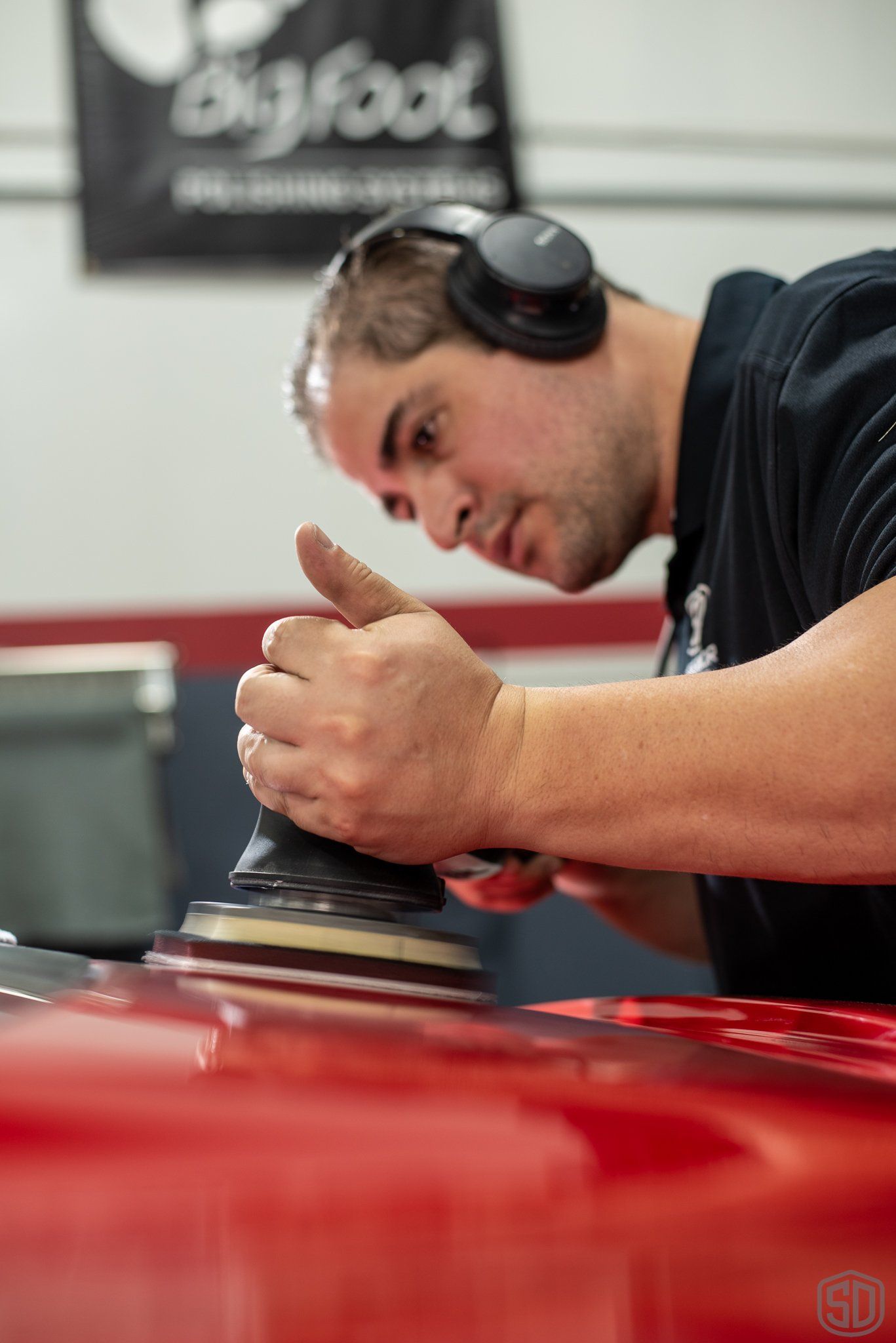 A man wearing headphones is polishing a red car.