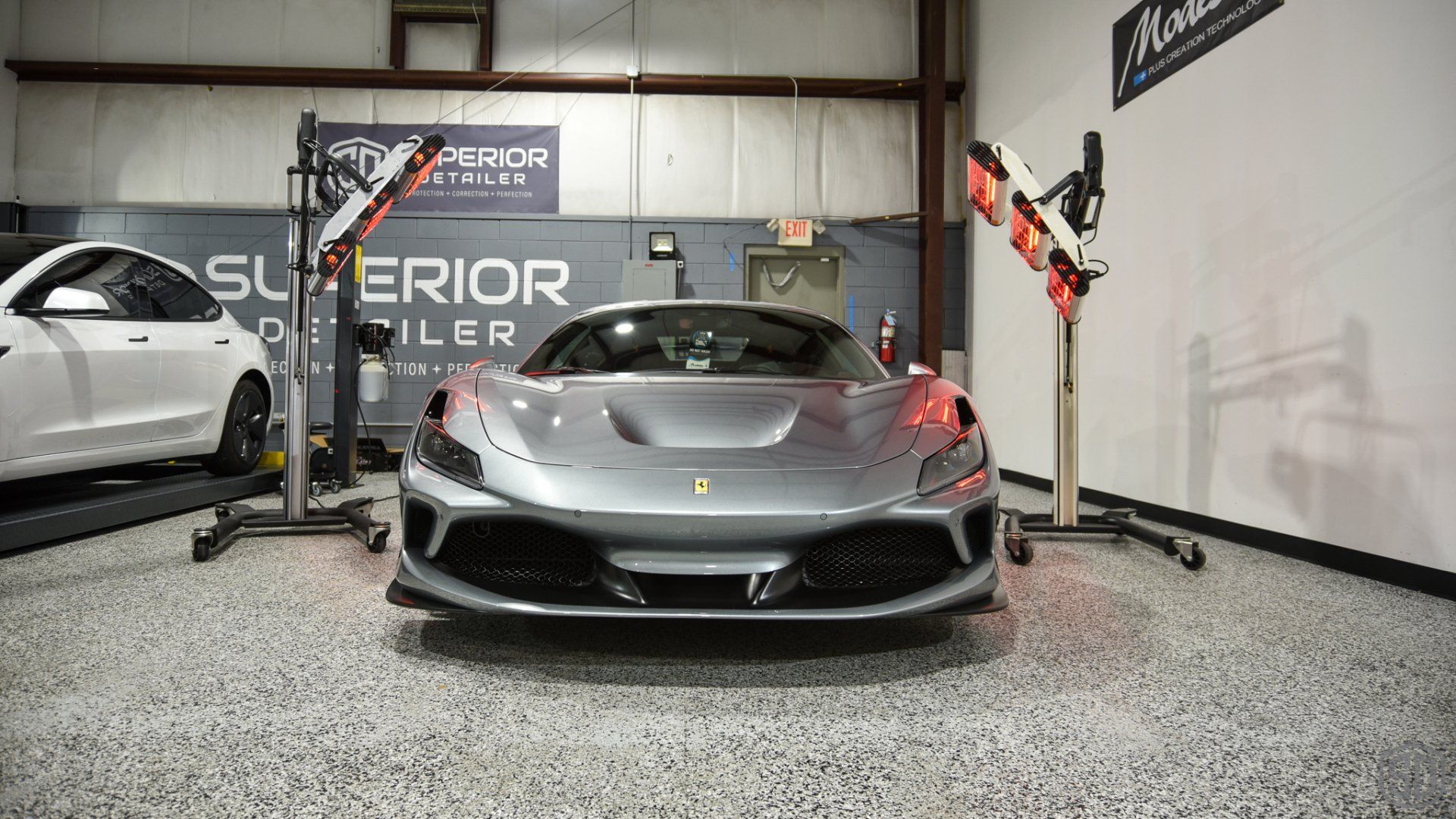 A gray sports car is parked in a garage next to a white car.