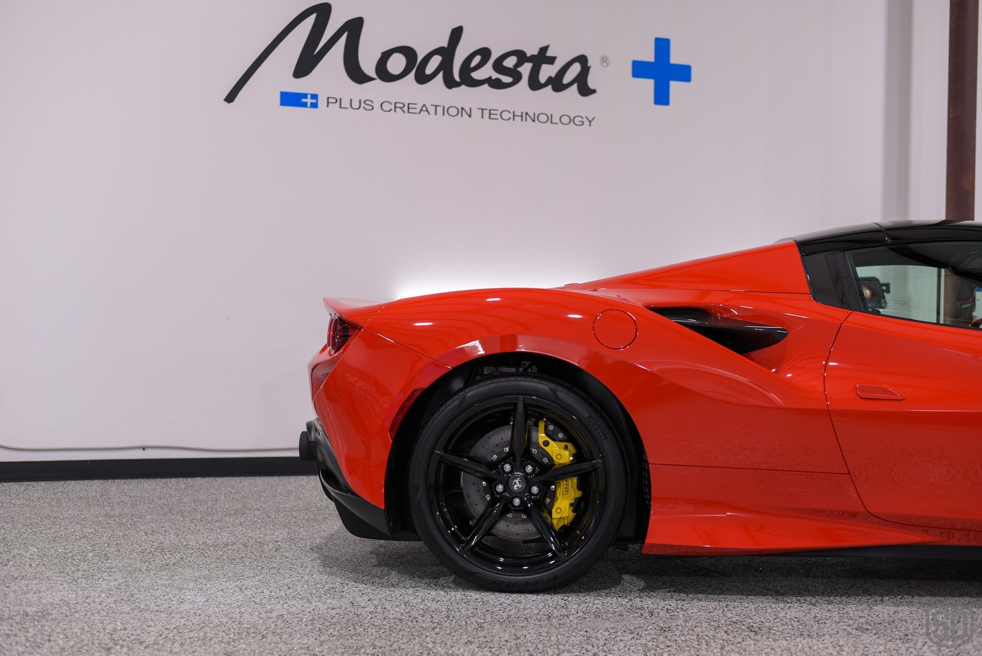 A red sports car is parked in front of a wall that says modesta