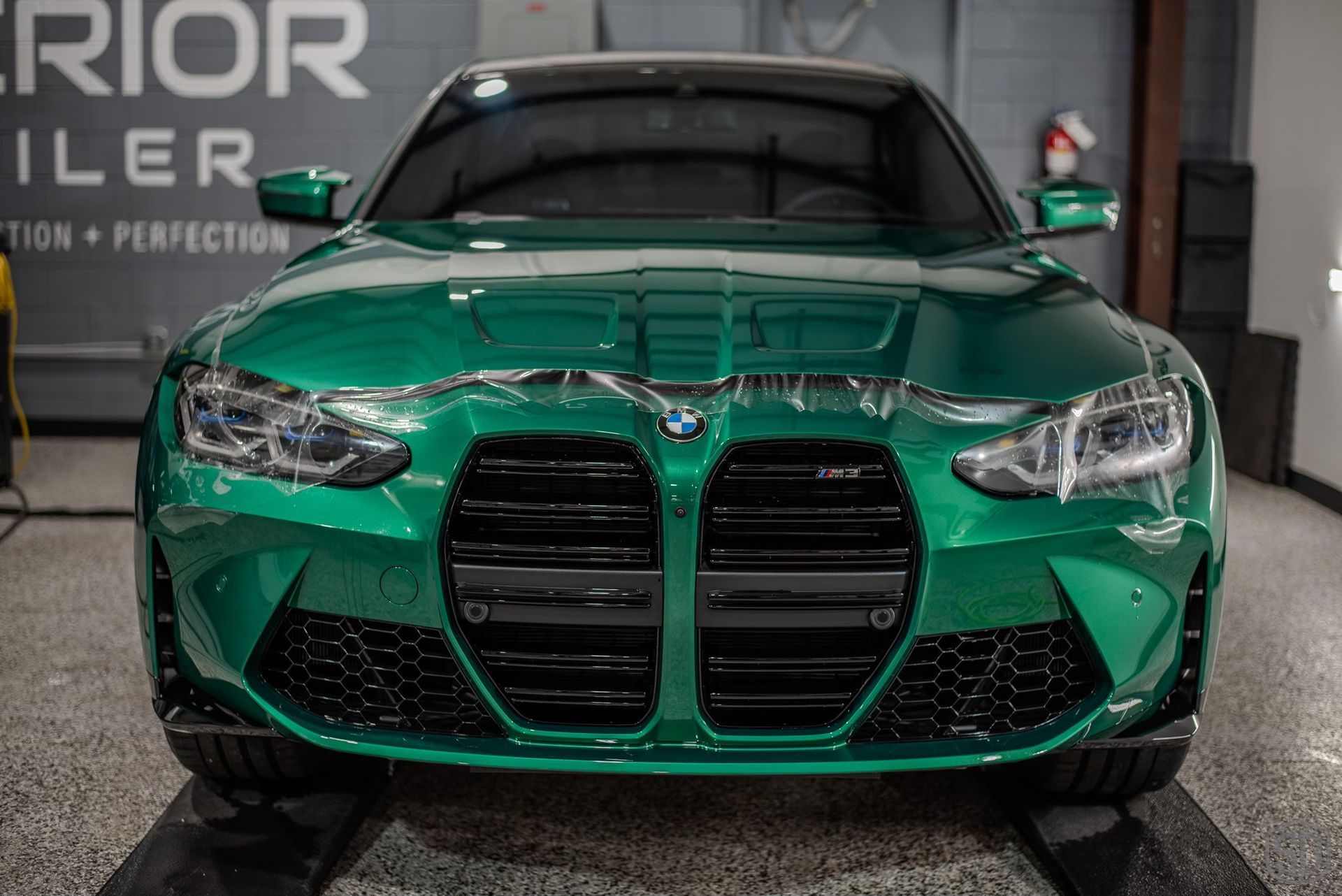 A green bmw m3 is wrapped in plastic in a garage.