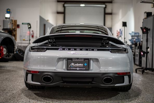 The rear end of a silver porsche 911 is parked in a garage.