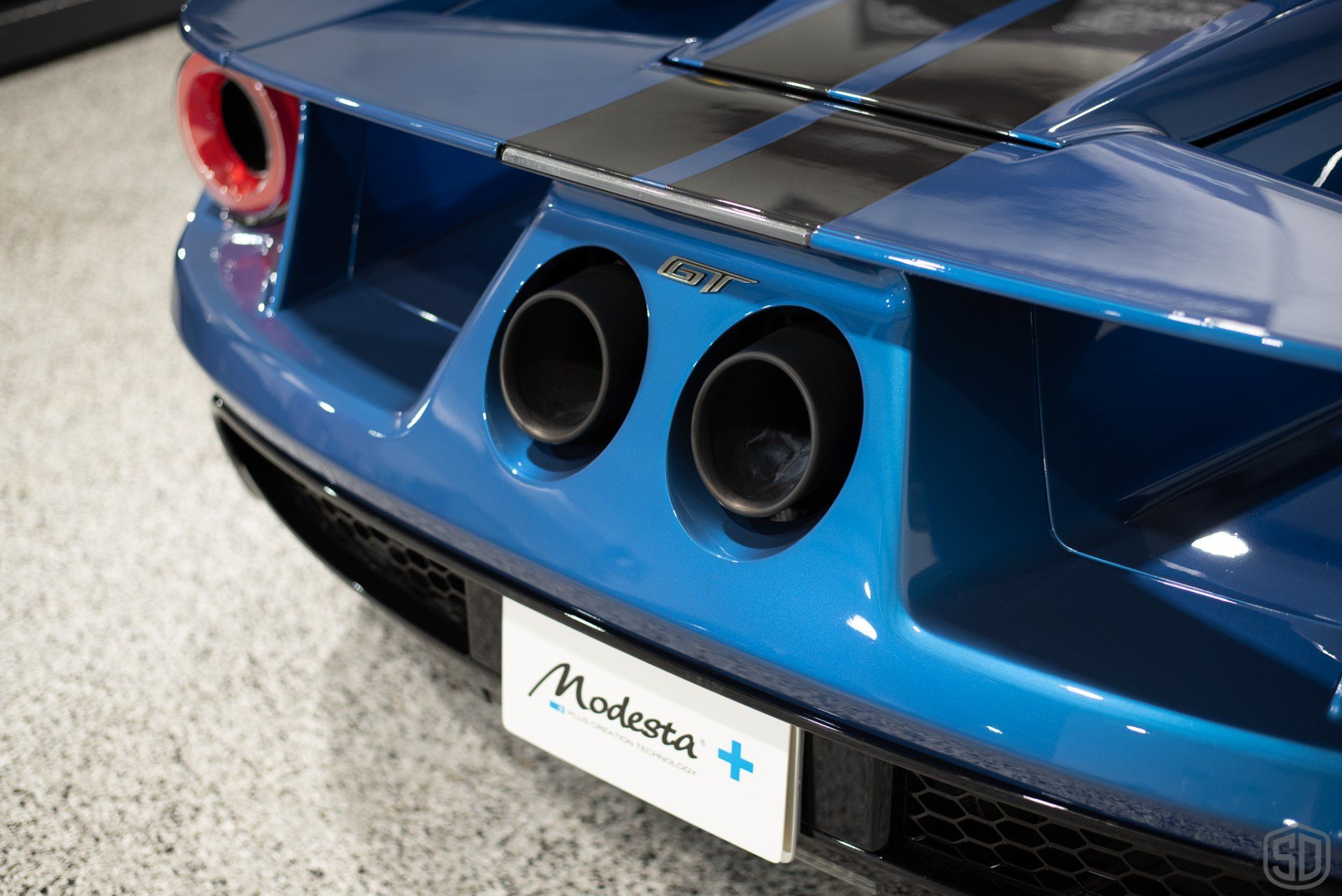 The rear end of a blue sports car with two exhaust pipes.