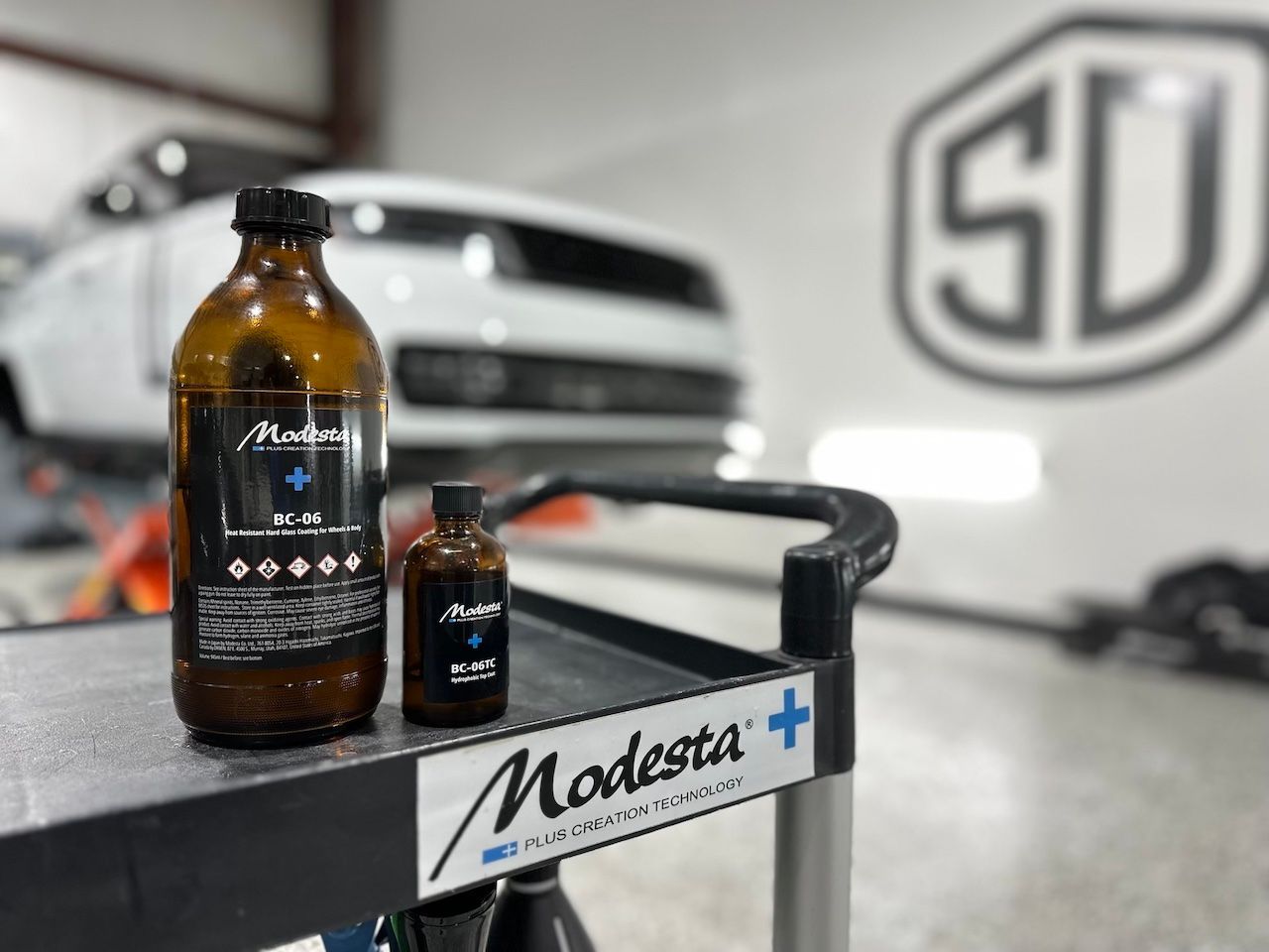 A bottle of polish is sitting on a cart in front of a white car.