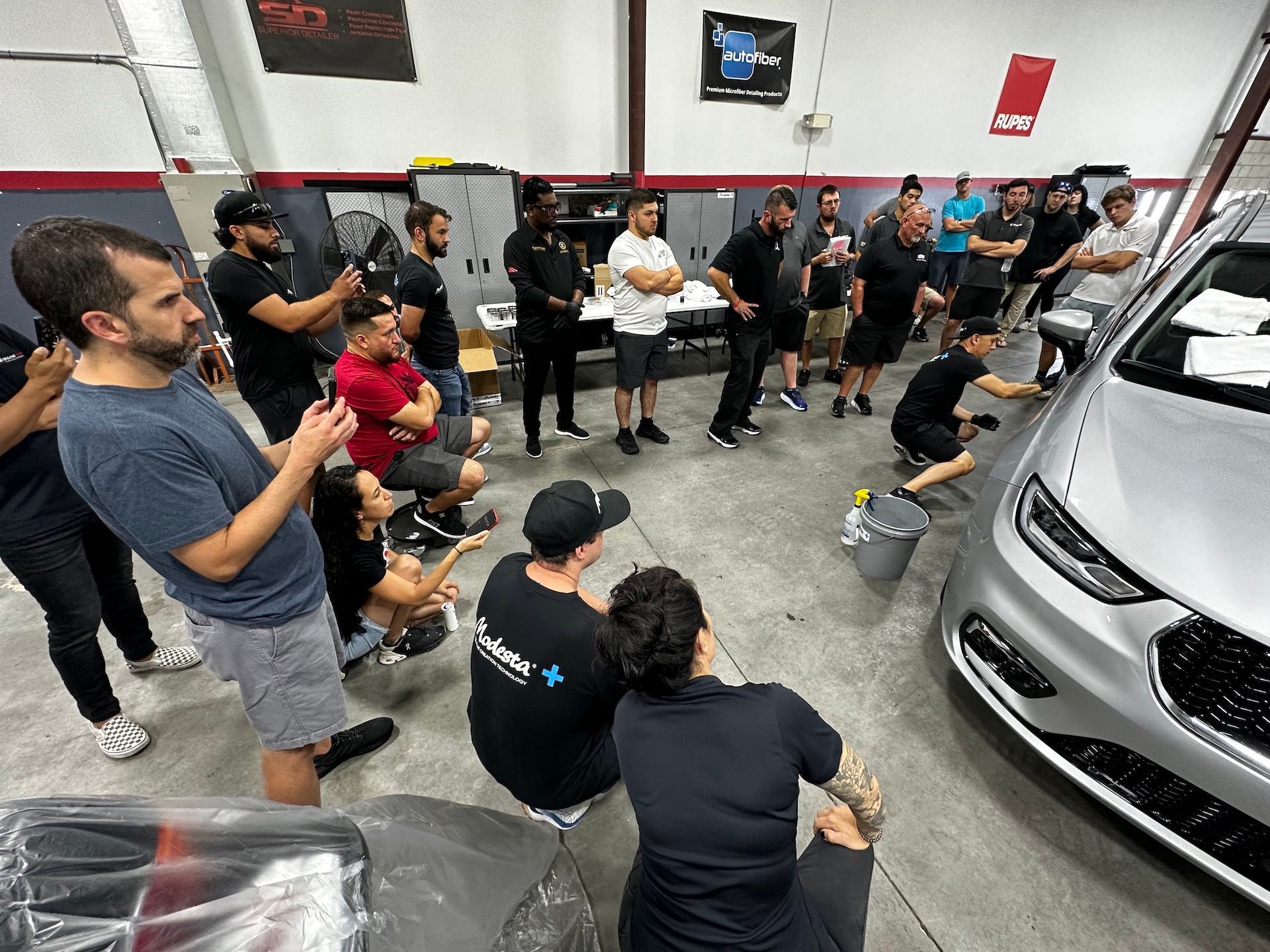 A group of people are standing around a car in a garage.