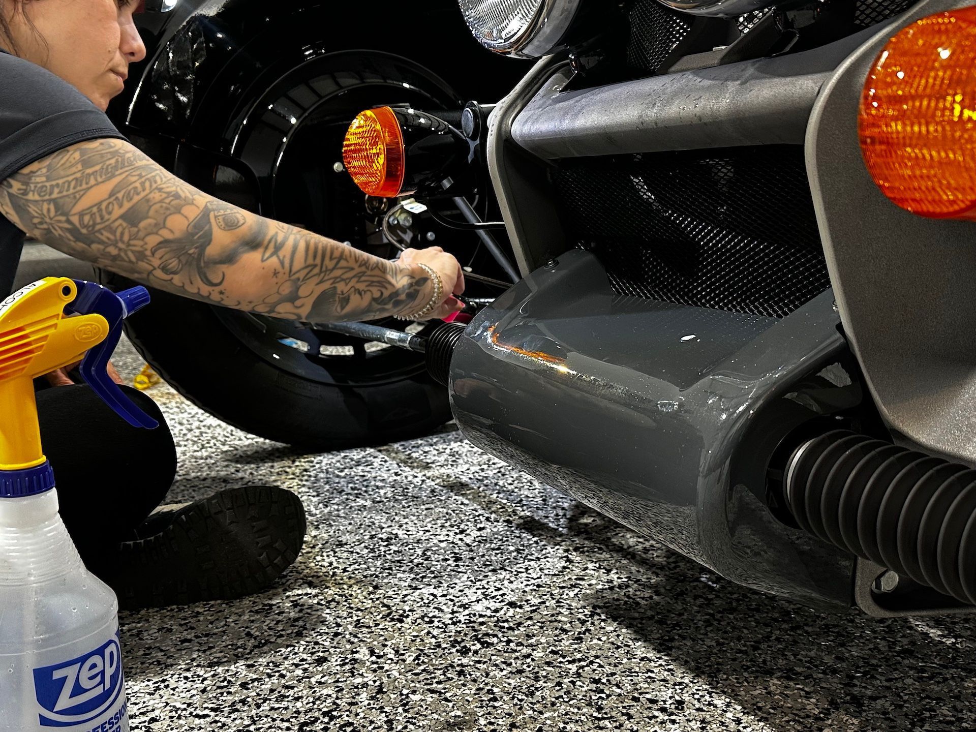 A woman is cleaning a motorcycle with a spray bottle that says 7up