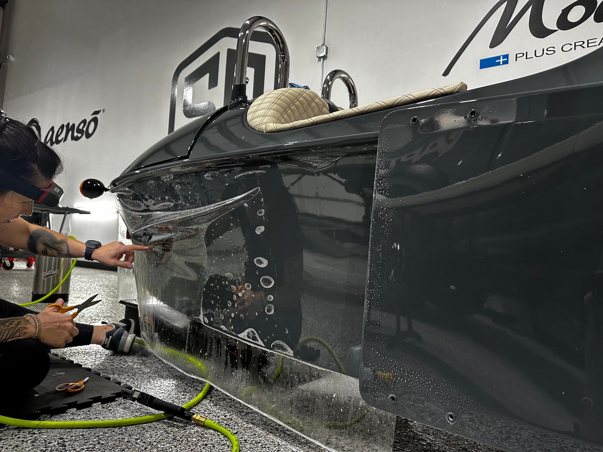 A man is cleaning a car with a hose in a garage.