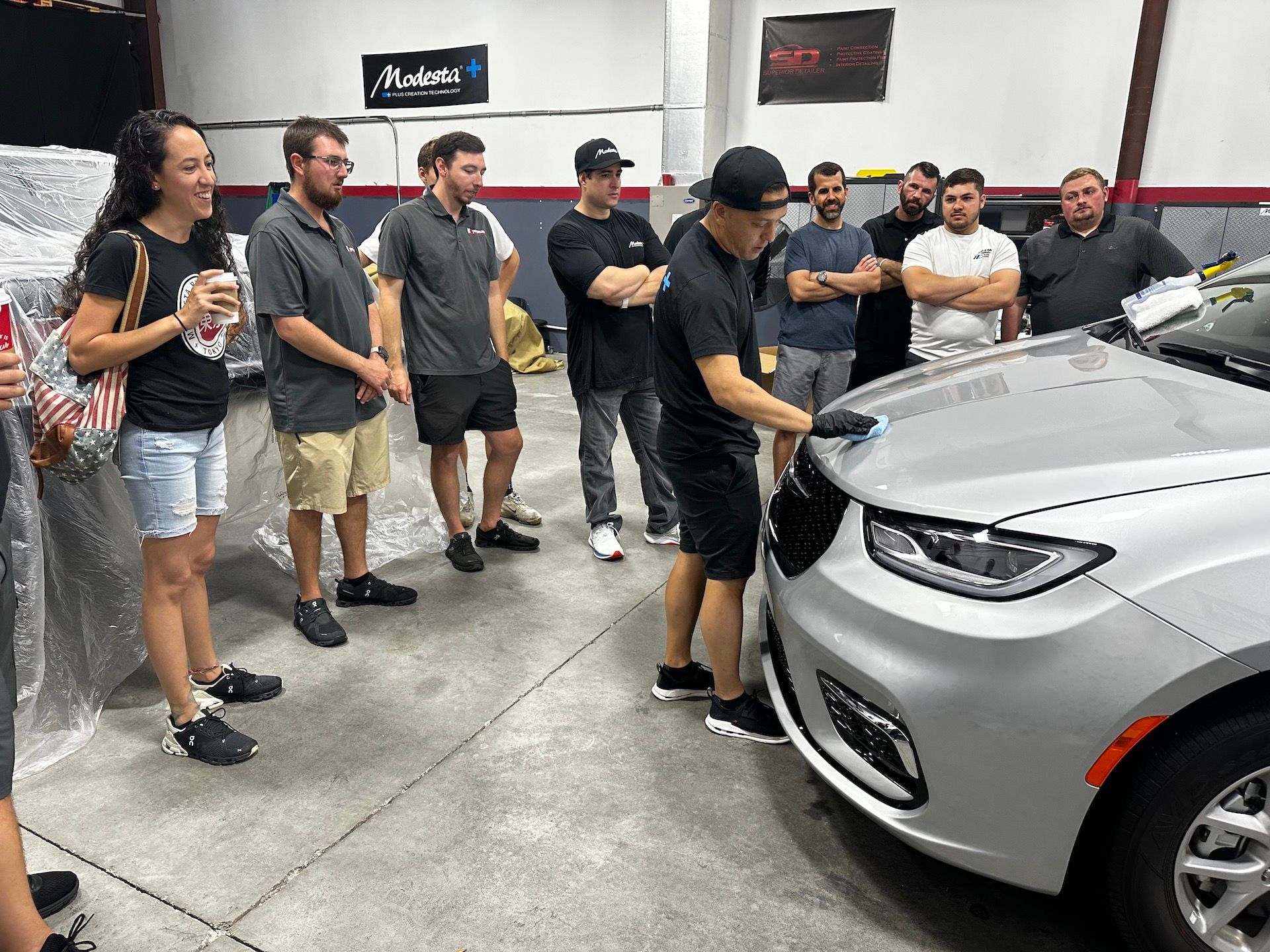 A group of people are standing around a car in a garage.