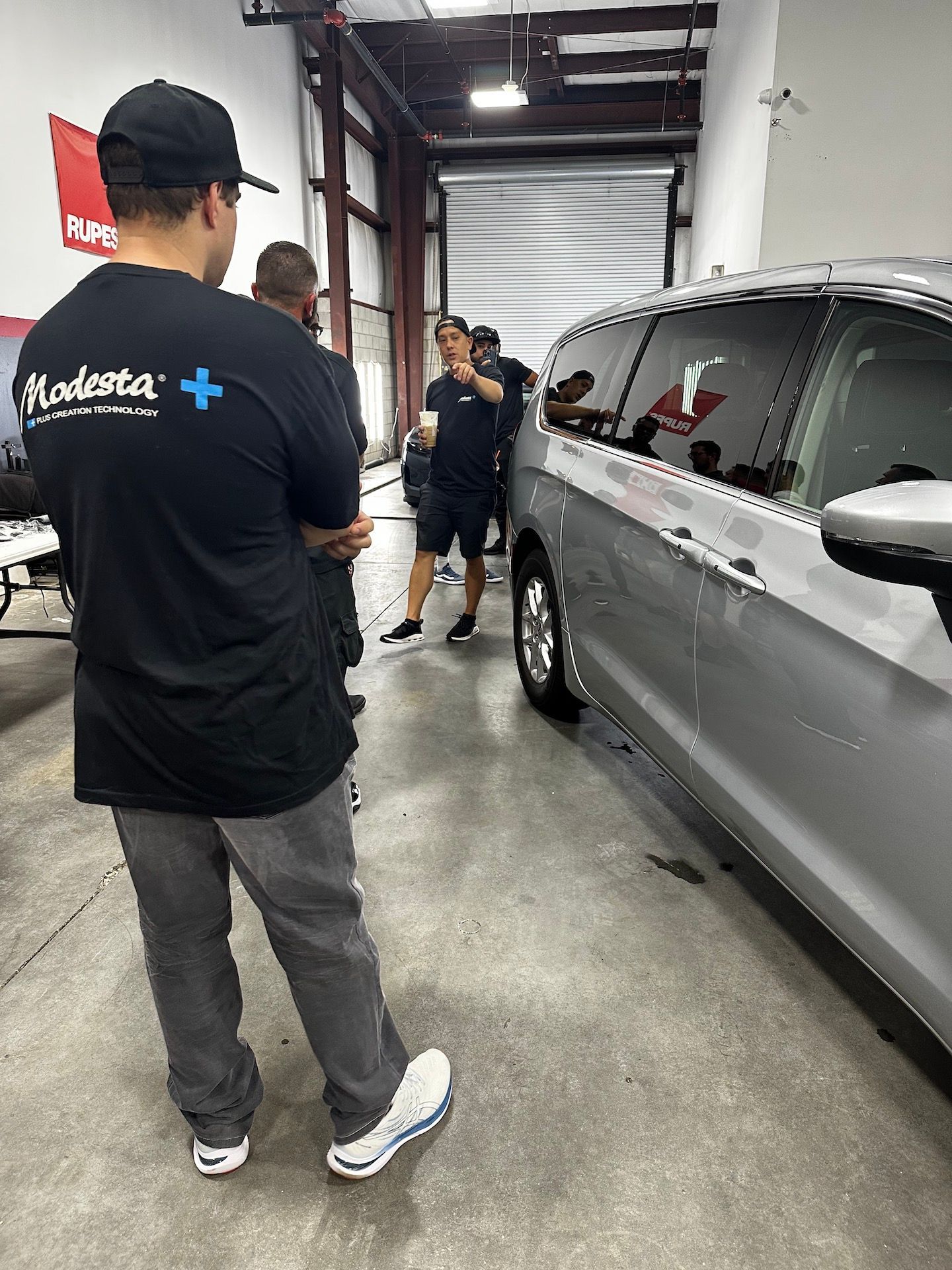 A man in a black shirt is standing next to a silver car in a garage.