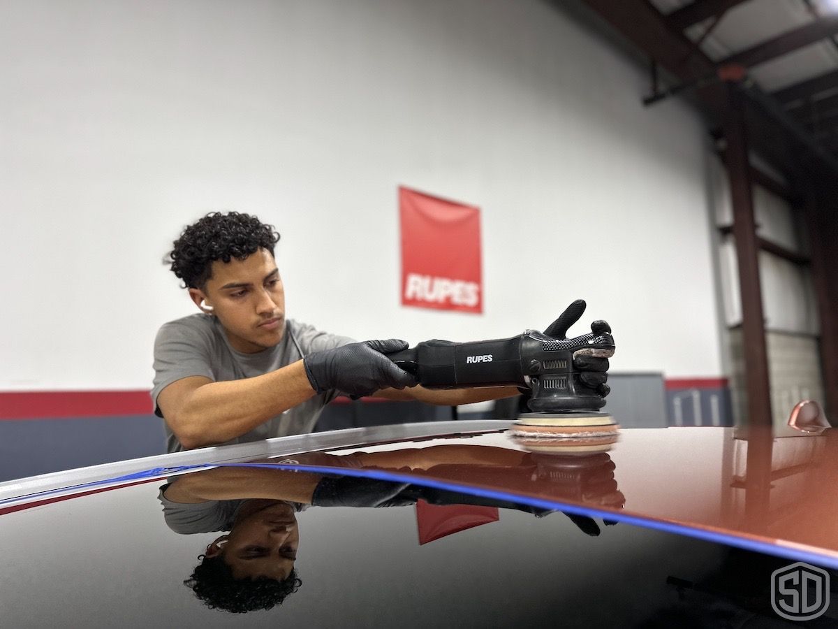 A man is polishing the roof of a car in a garage.